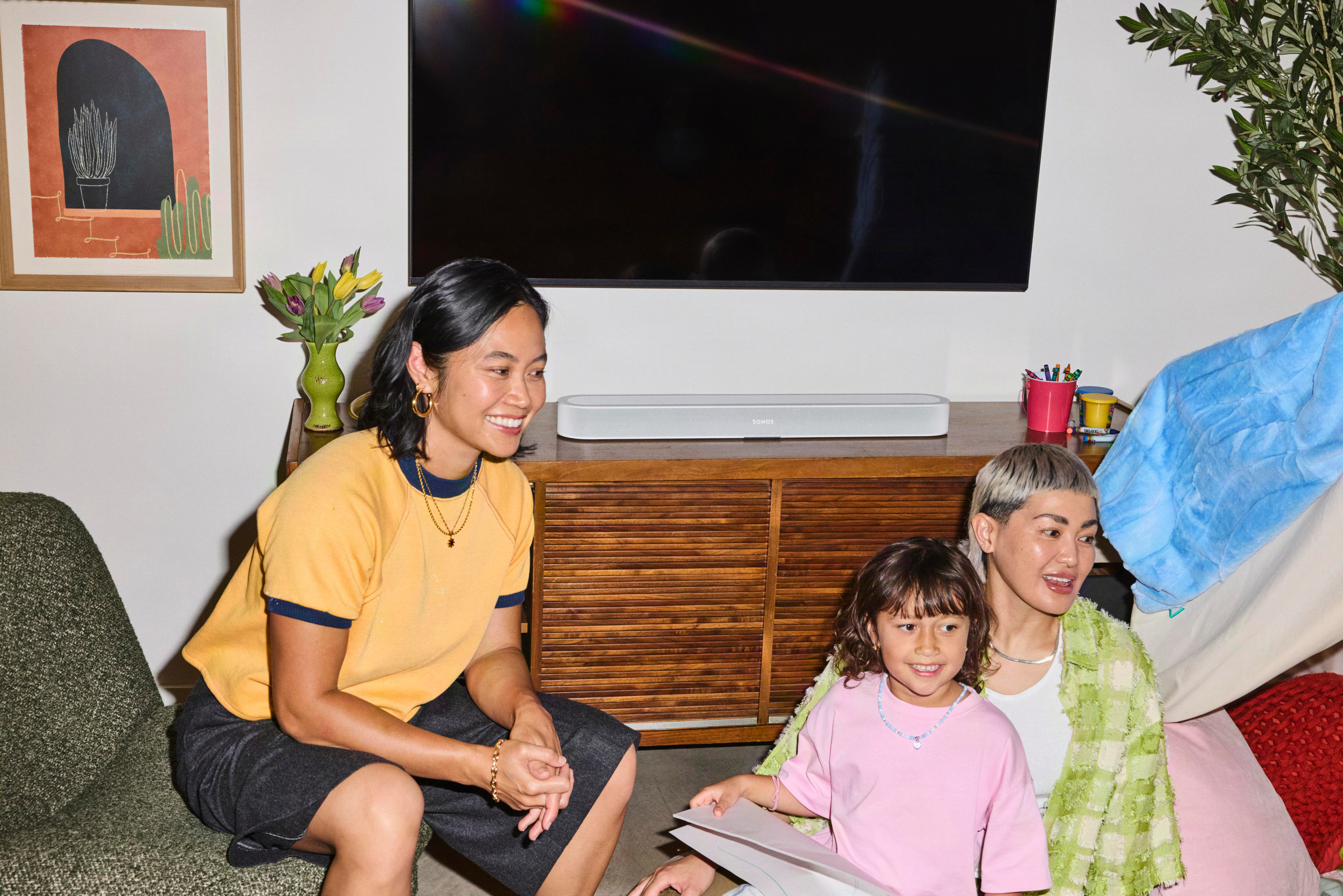 Eine asiatische Familie sitzt lächelnd in einem Wohnzimmer vor einem Fernseher.