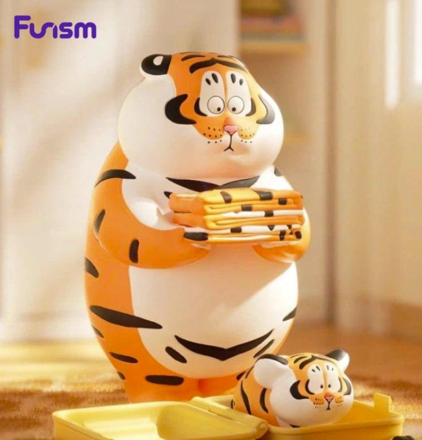 Eine dicke Plüsch-Tigerfigur hält einen kleinen Turm aus Tiger-Mustern in den Händen, während ein kleiner Tiger daneben sitzt.