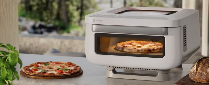 Egy fehér Electrolux sütő pulton, benne egy pizzával és mellette egy másikkal.