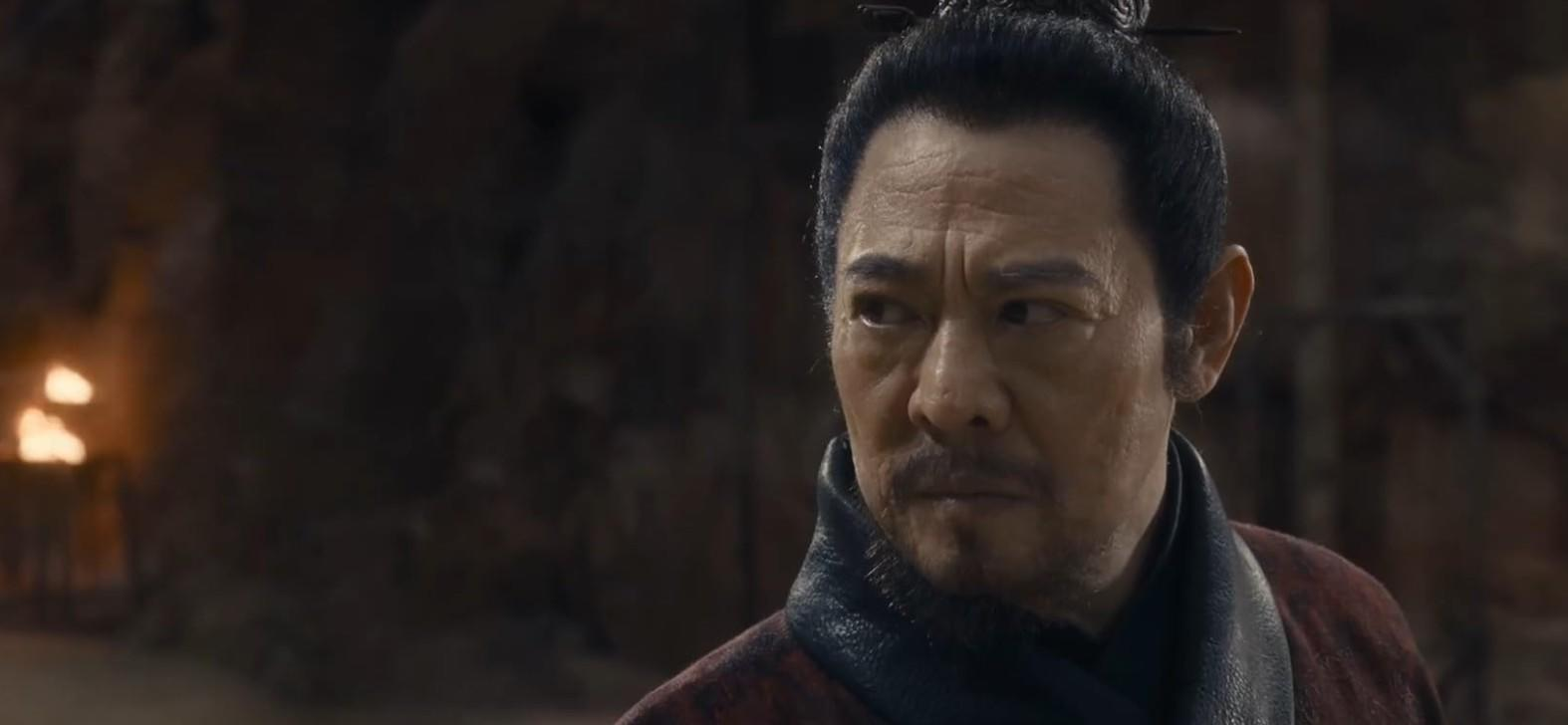 Ein asiatischer Mann mittleren Alters mit dunklem Haar und dunkler Kleidung schaut wachsam zur Seite.