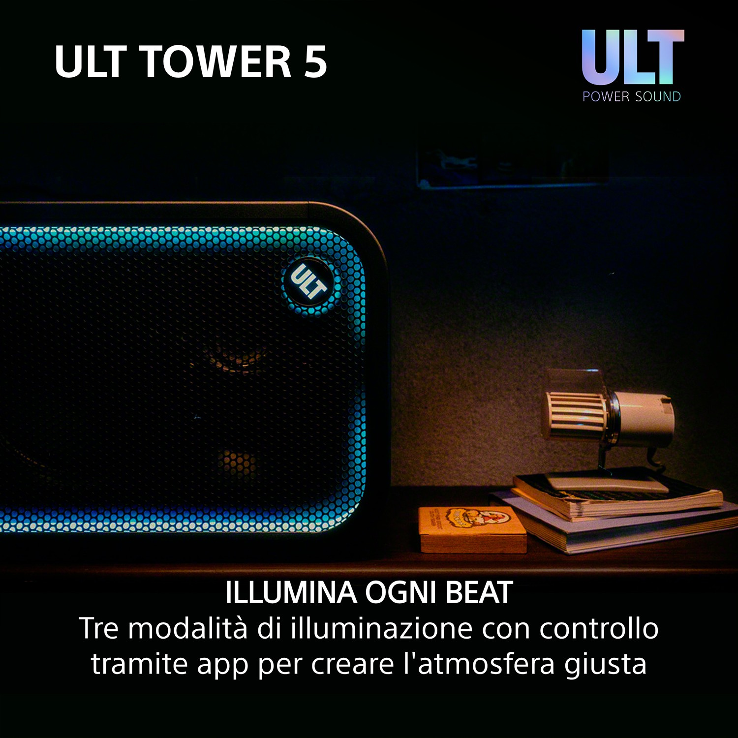 Un altoparlante ULT Tower 5 con illuminazione blu è su un tavolo accanto a libri e una piccola lampada.