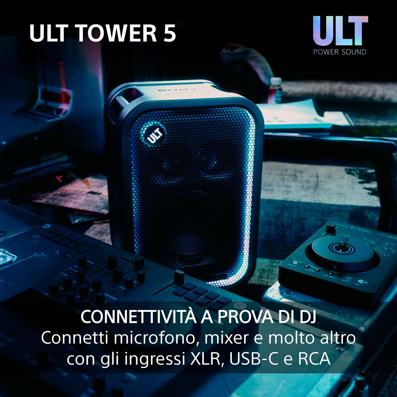 Speaker Ult Tower 5 in una stanza poco illuminata con attrezzatura da DJ in primo piano e luce blu.