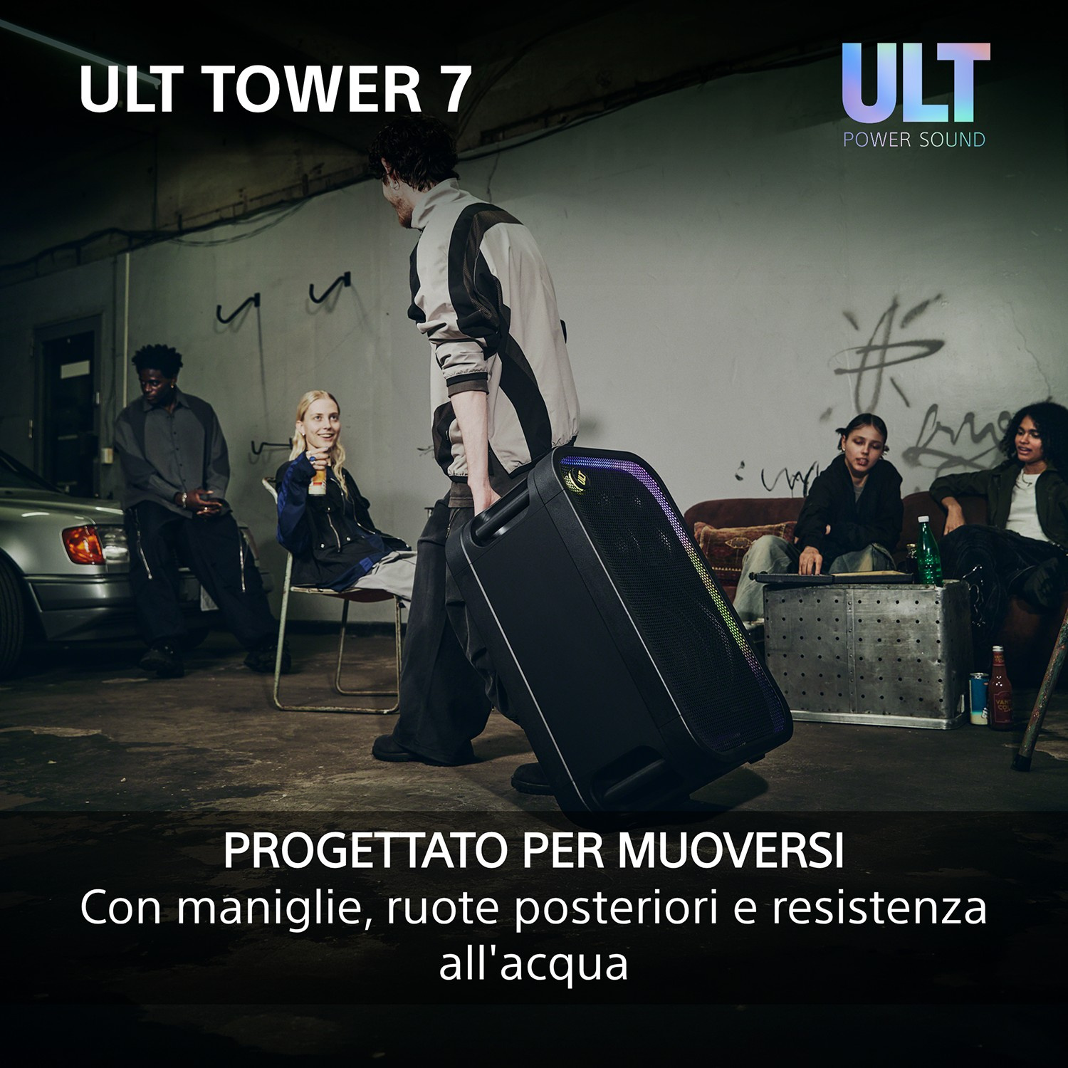 Una persona trascina un grande altoparlante nero ULT Tower 7 con ruote in una stanza con altre persone.