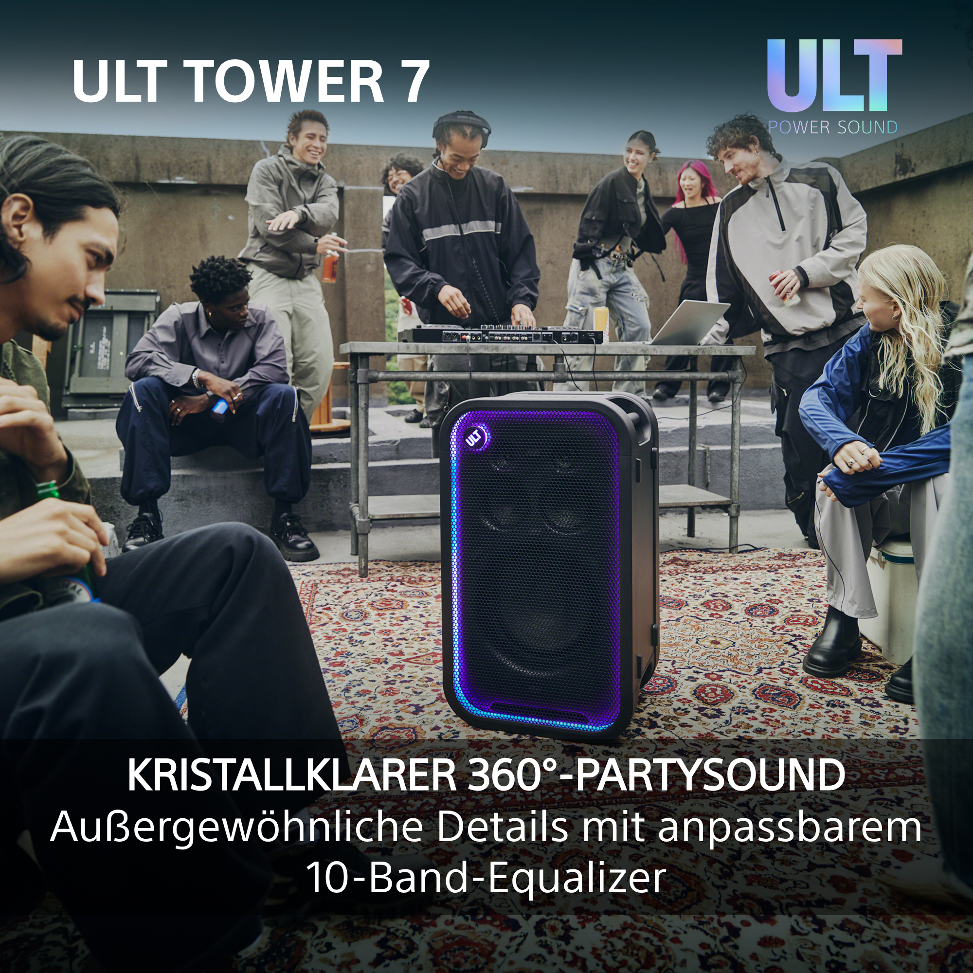 Eine Gruppe junger Leute versammelt sich auf einer Dachterrasse um einen großen, beleuchteten Party-Lautsprecher.