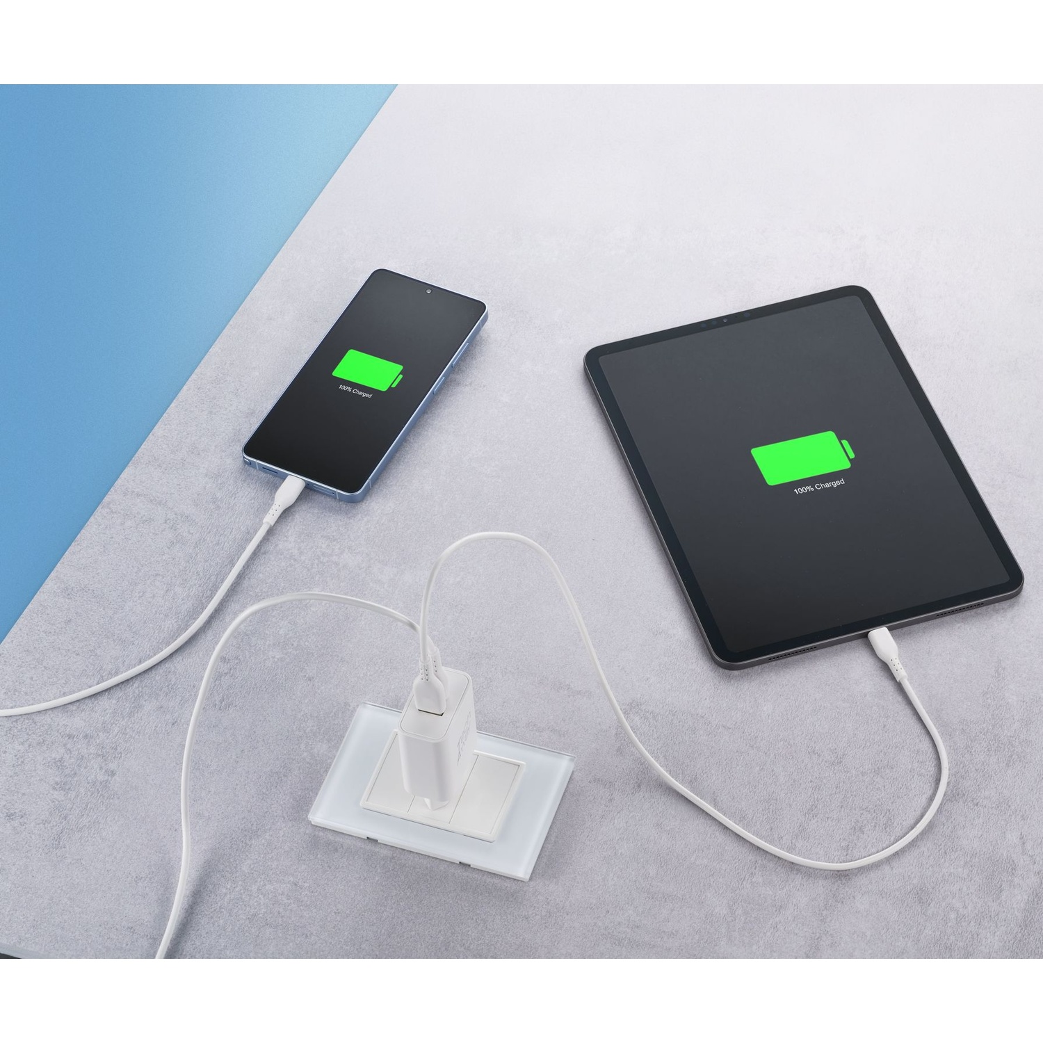 Uno smartphone e un tablet sono collegati contemporaneamente a un caricatore a muro bianco su una superficie grigia.