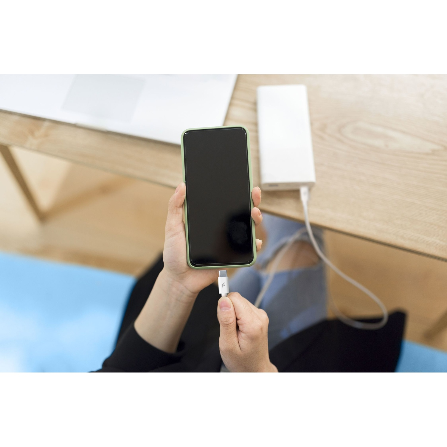Una persona che carica uno smartphone con un power bank su una scrivania di legno.