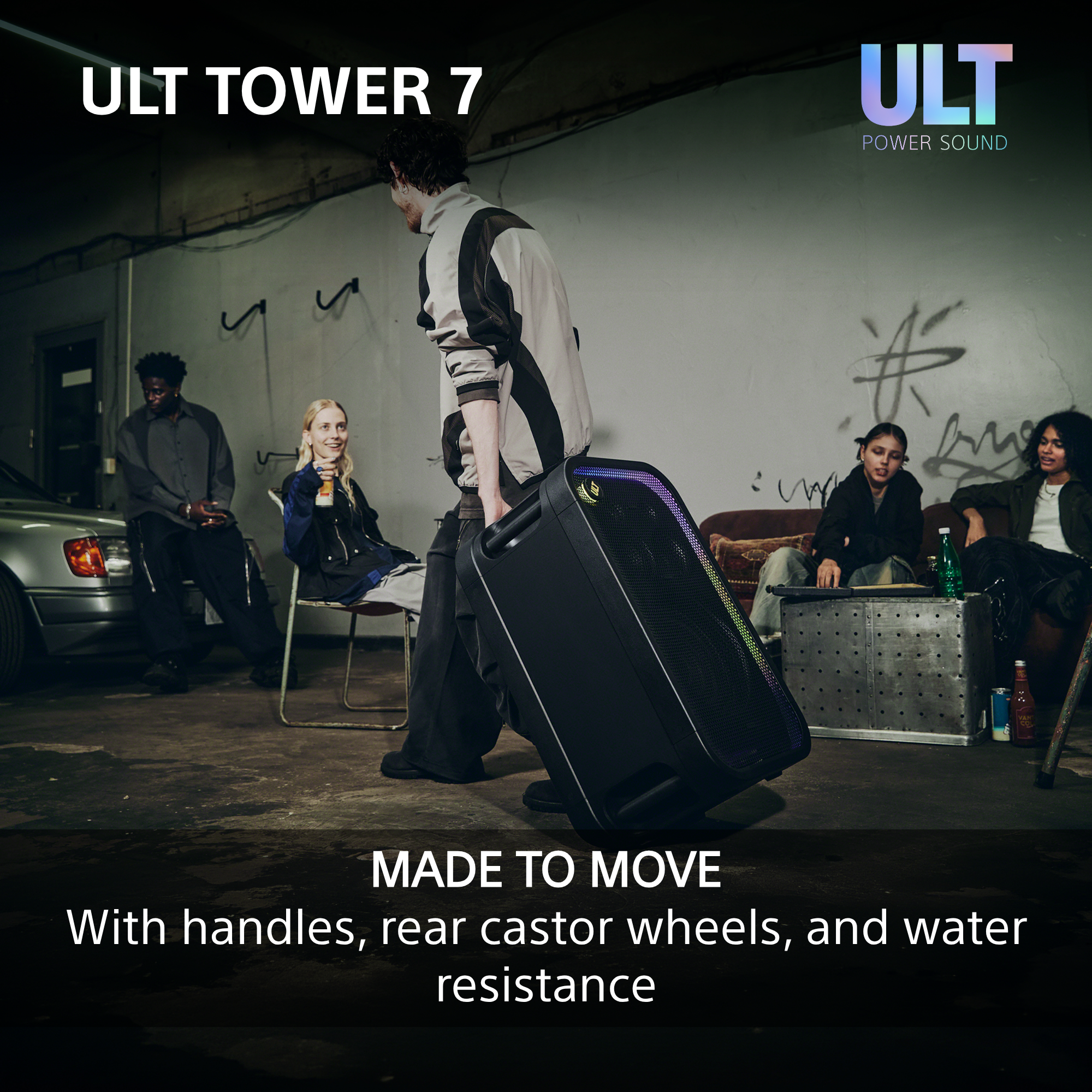 Ein Mann zieht einen großen schwarzen ULT Tower 7 Lautsprecher in einem urbanen Raum mit vier sitzenden Personen.