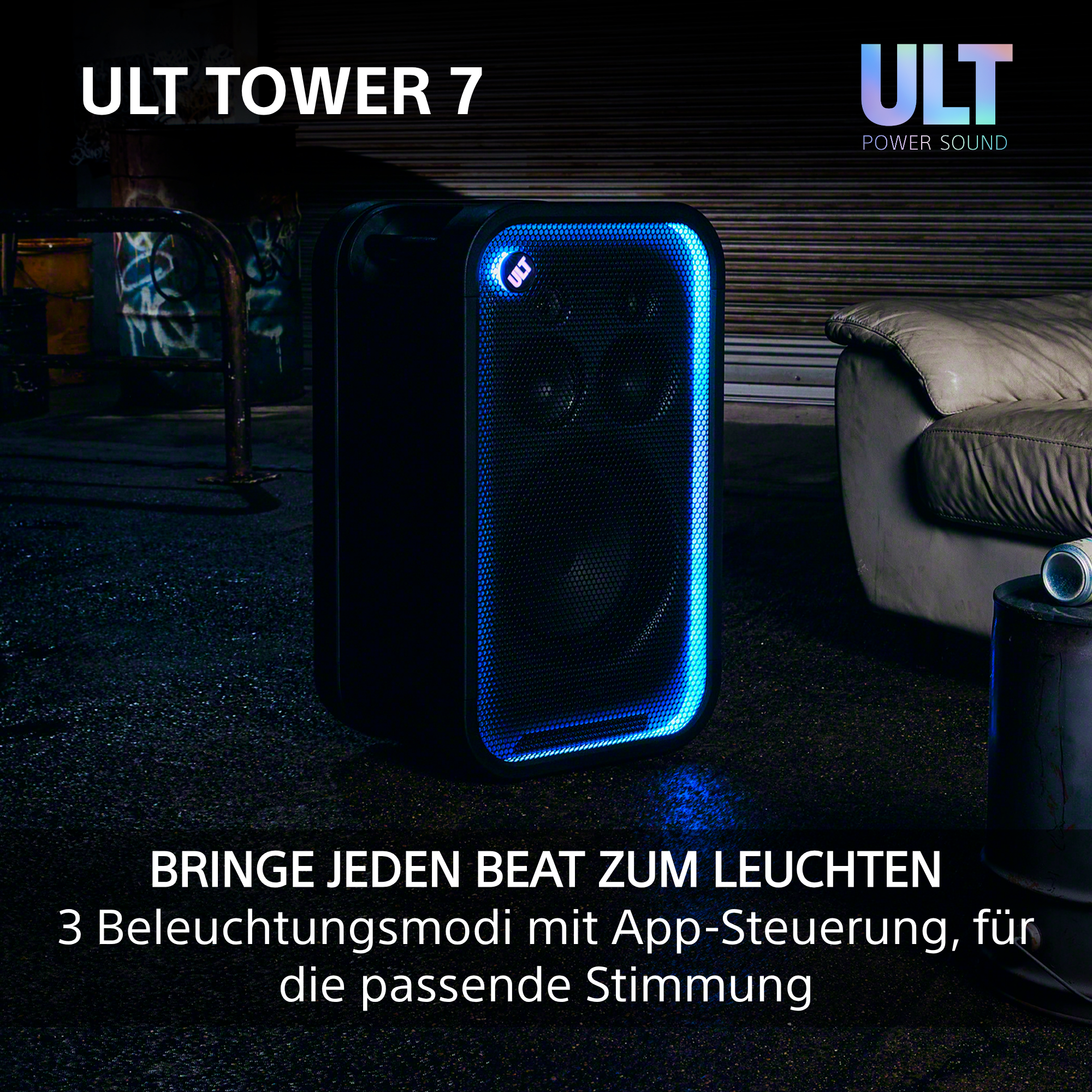 Ein schwarzer ULT Tower 7 Lautsprecher leuchtet in einem dunklen Raum blau neben einem Sofa.