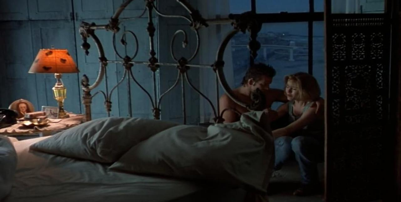 Ein Mann und eine Frau sitzen in einem gedimmten Raum mit Schmiedeeisenbett am Fenster.