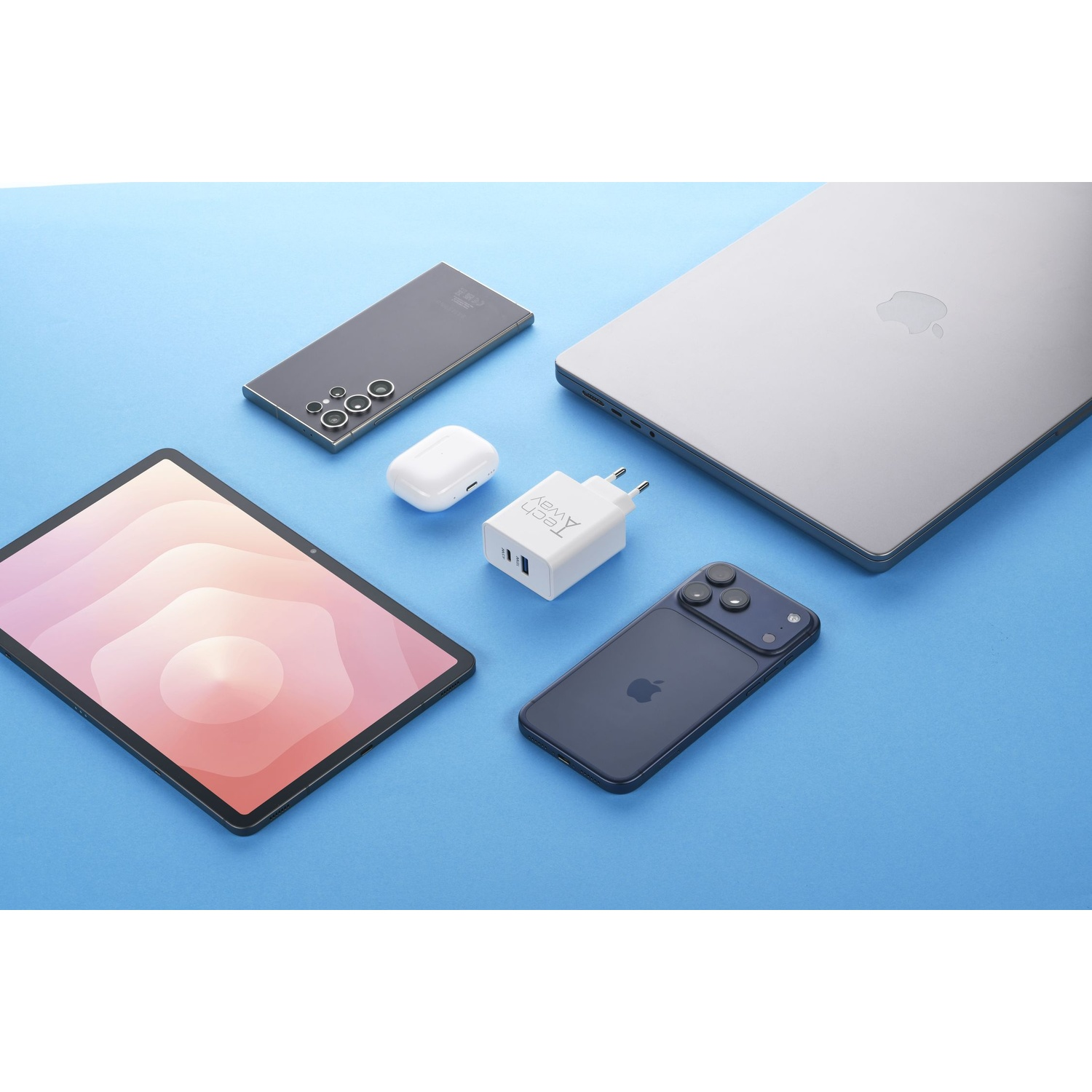 Vari dispositivi tecnologici come laptop, smartphone, tablet e caricatore disposti su sfondo azzurro.