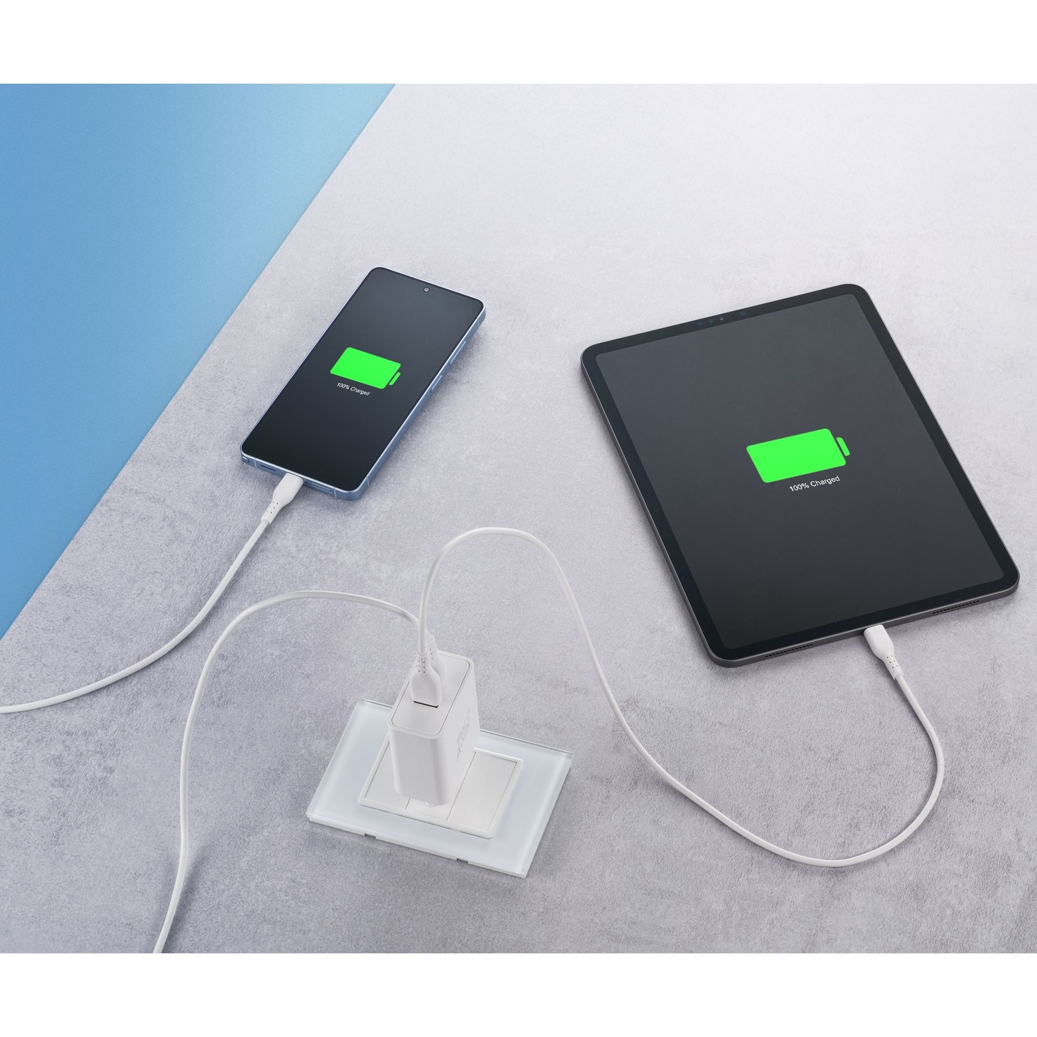 Uno smartphone e un tablet in carica da un caricabatterie bianco a muro.