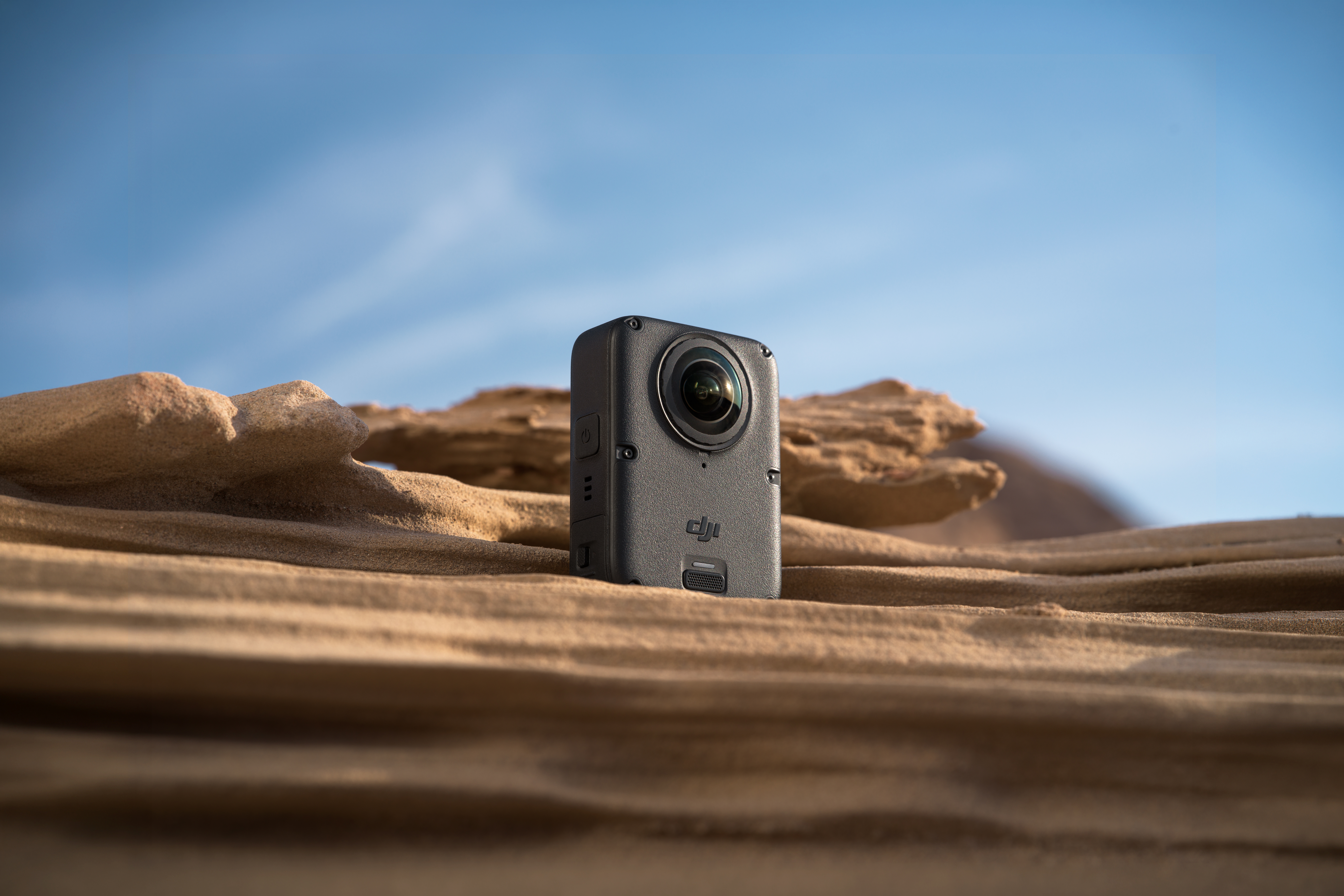 Eine kleine schwarze DJI-Kamera steht auf sandigen Felsen vor einem blauen Himmel.