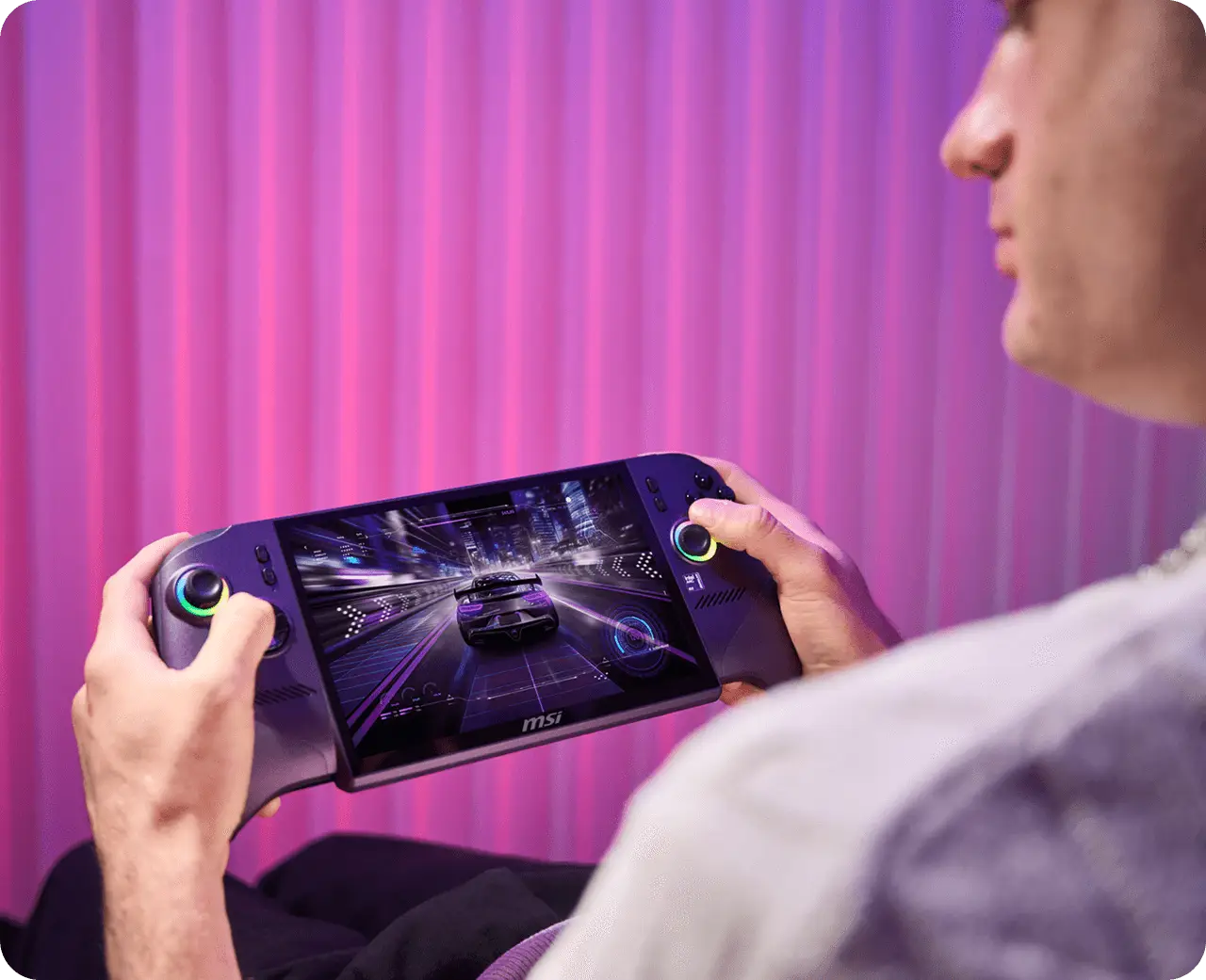 Un uomo gioca a un gioco di corse su una console portatile con sfondo rosa.