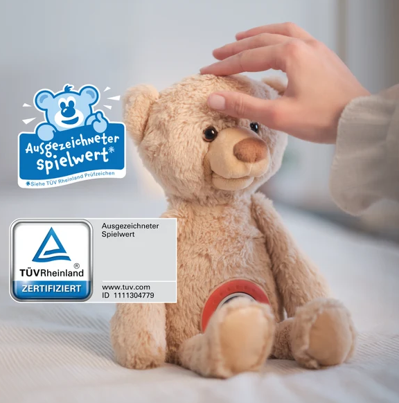 Hand berührt den Kopf eines Plüschbären, mit TÜV-Siegel.