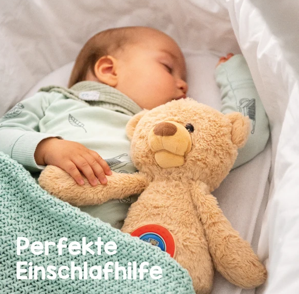 Ein Baby schläft friedlich im Bettchen und hält einen Plüschbären neben einer mintgrünen Decke.
