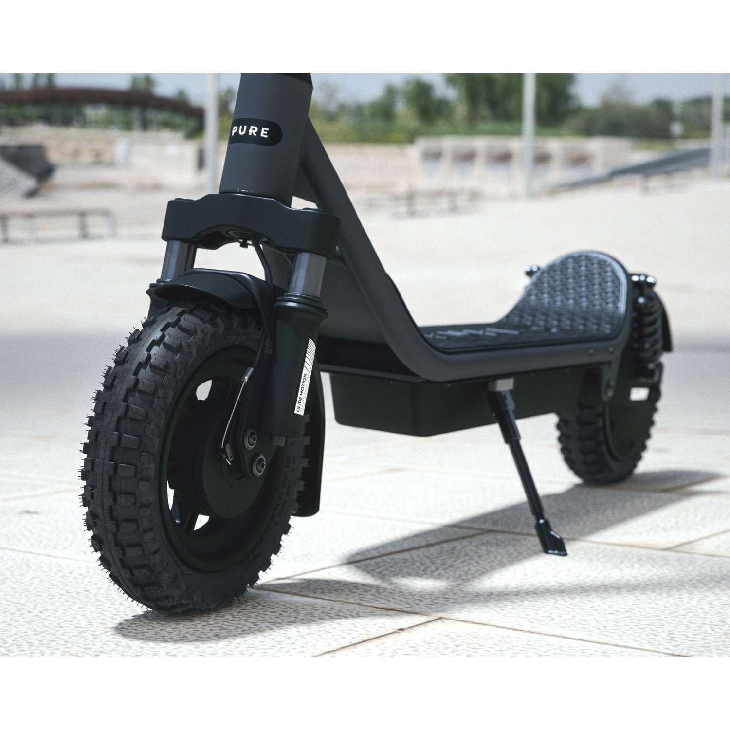 A black Pure electric scooter with off-road tires parked on a tiled outdoor ground with a blurred background.