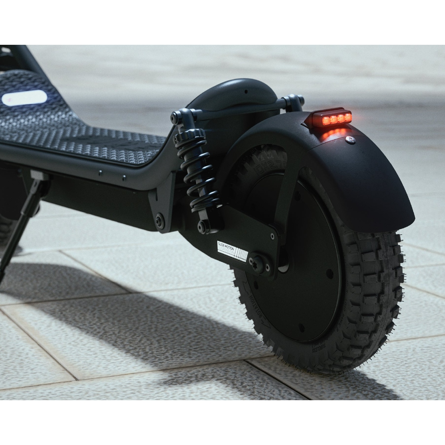 Close-up of the rear wheel, suspension, and glowing red taillight of a black electric scooter on a paved walkway.