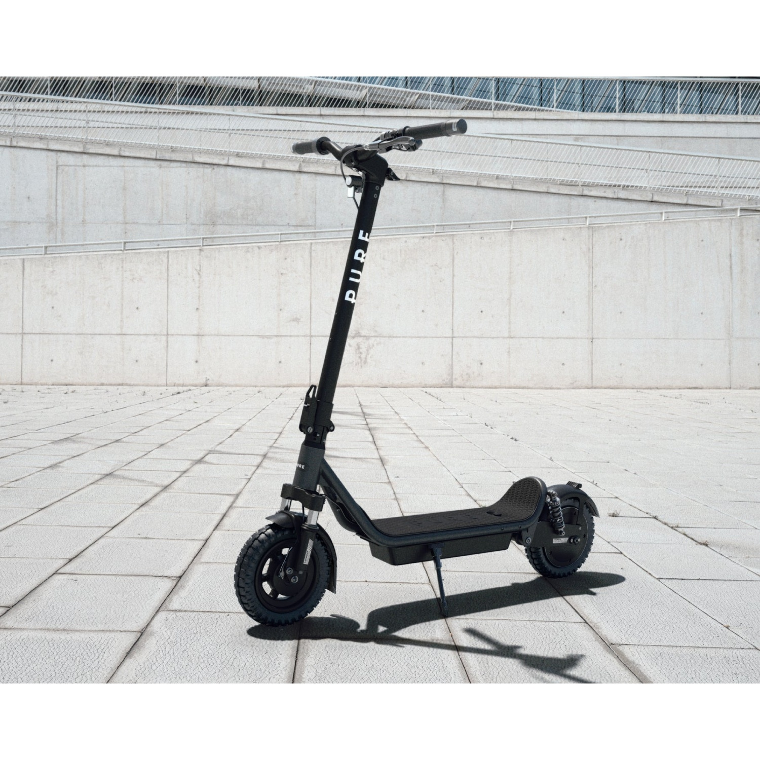 A black electric scooter with the PURE logo stands on a paved ground against a modern concrete building.