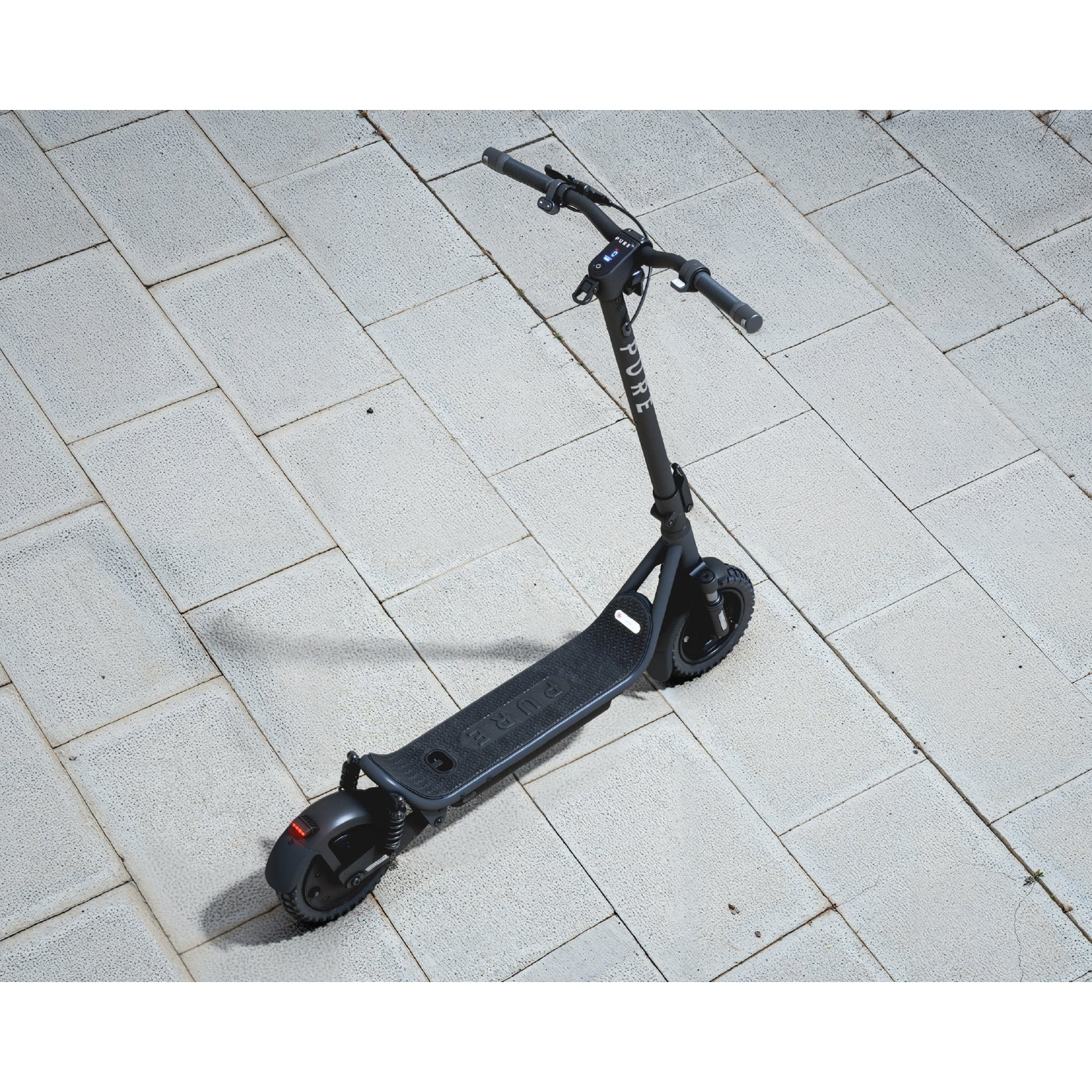 A black electric scooter stands on a grey paved stone ground.
