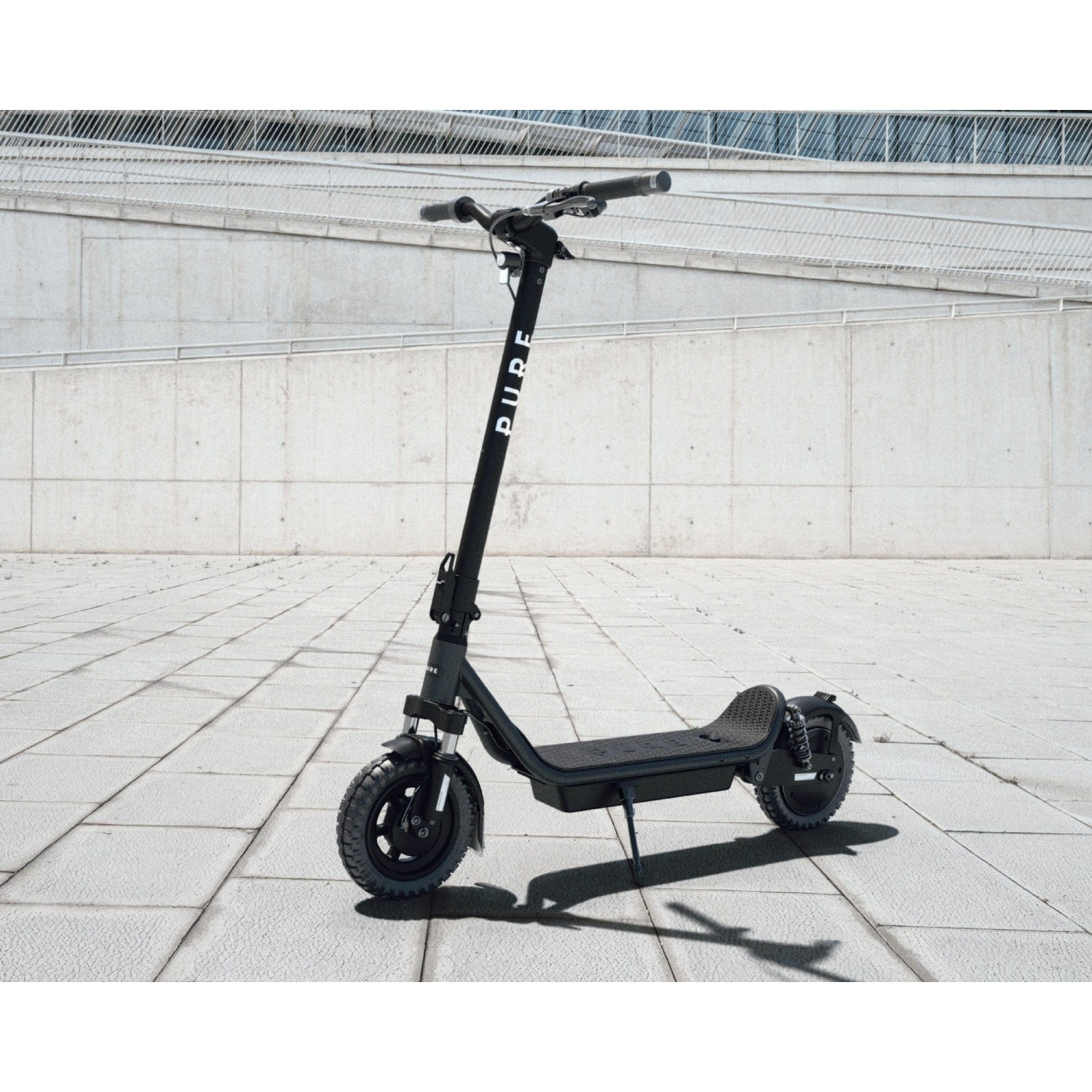A black electric scooter parked on a tiled plaza in front of a modern concrete wall.