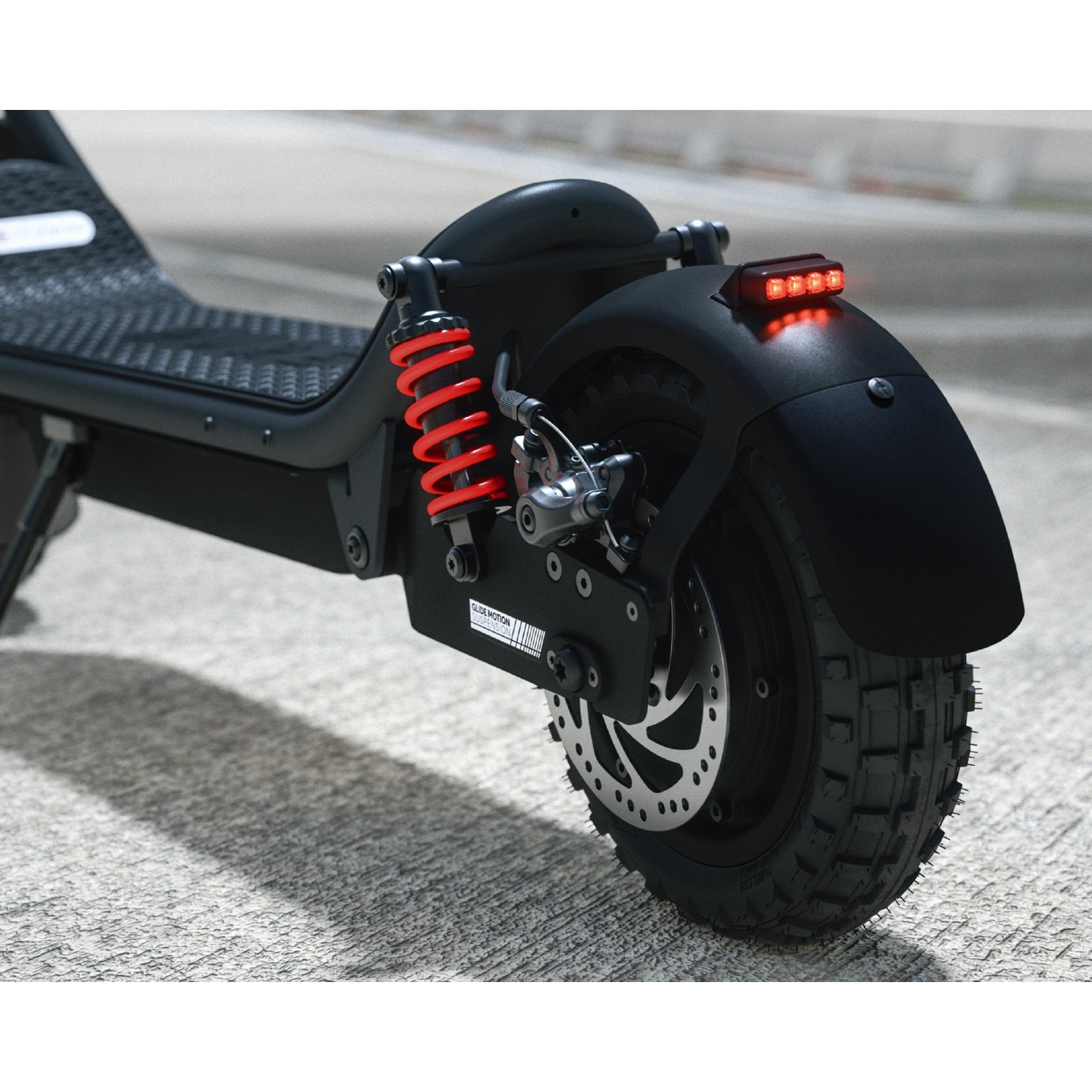 Rear view of a black electric scooter with red suspension, disc brake, and glowing tail light.