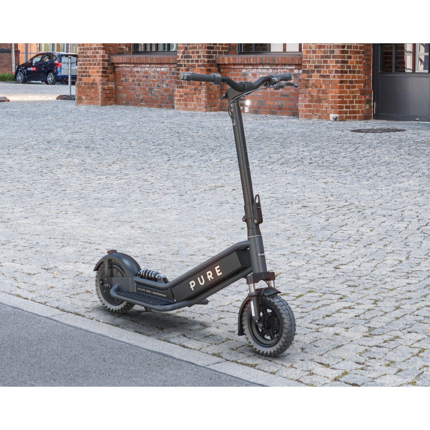 A black Pure electric scooter parked on a cobblestone street in front of a brick building.