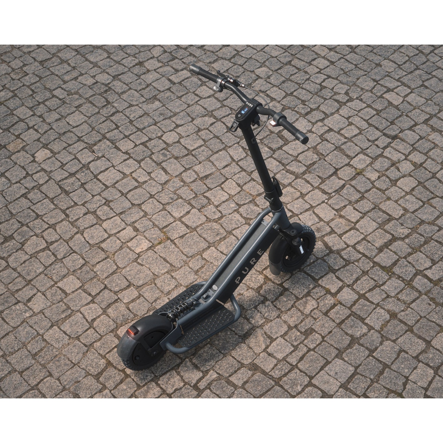 A gray electric scooter stands on a gray cobblestone ground.