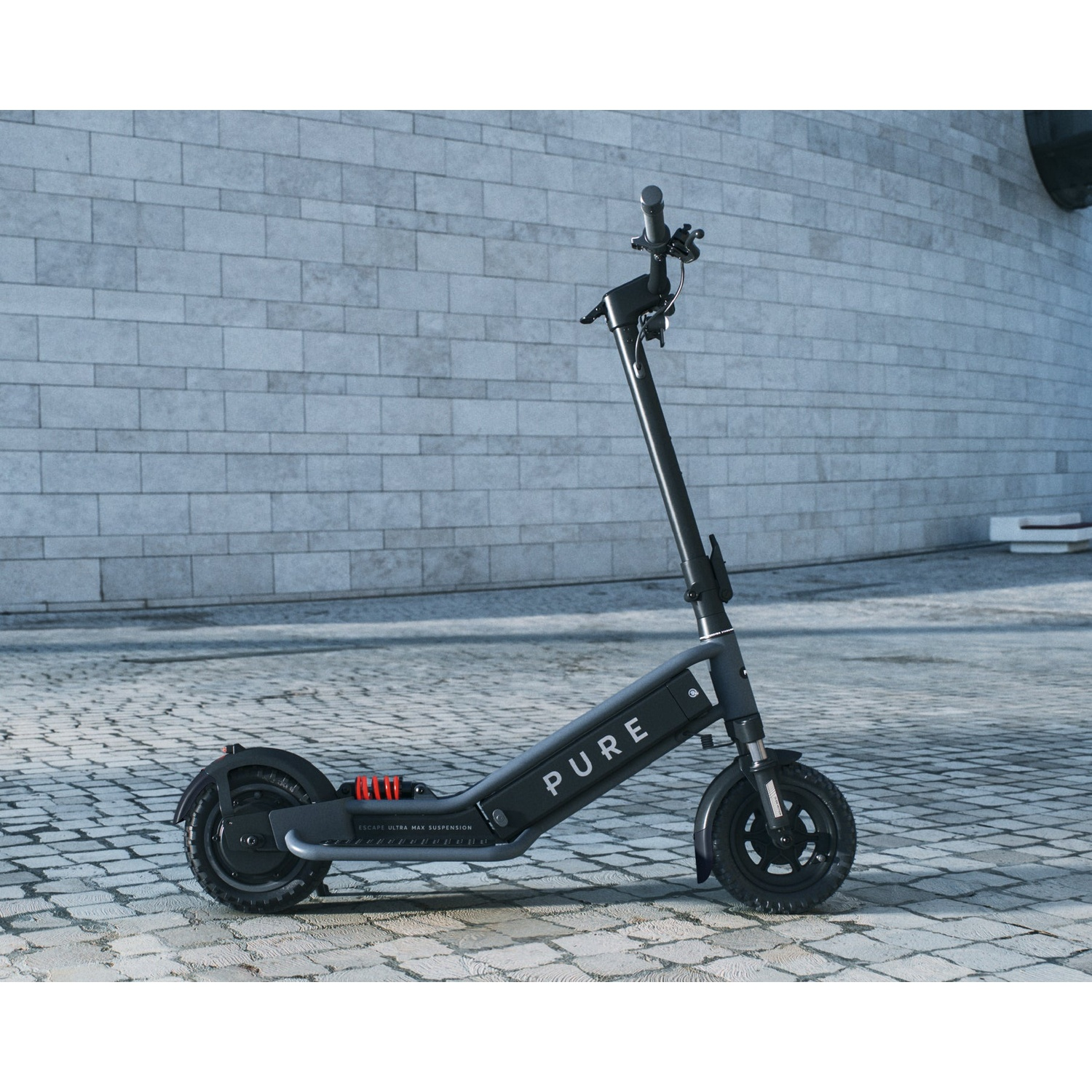 A black Pure electric scooter stands on a cobblestone pavement in front of a stone wall.