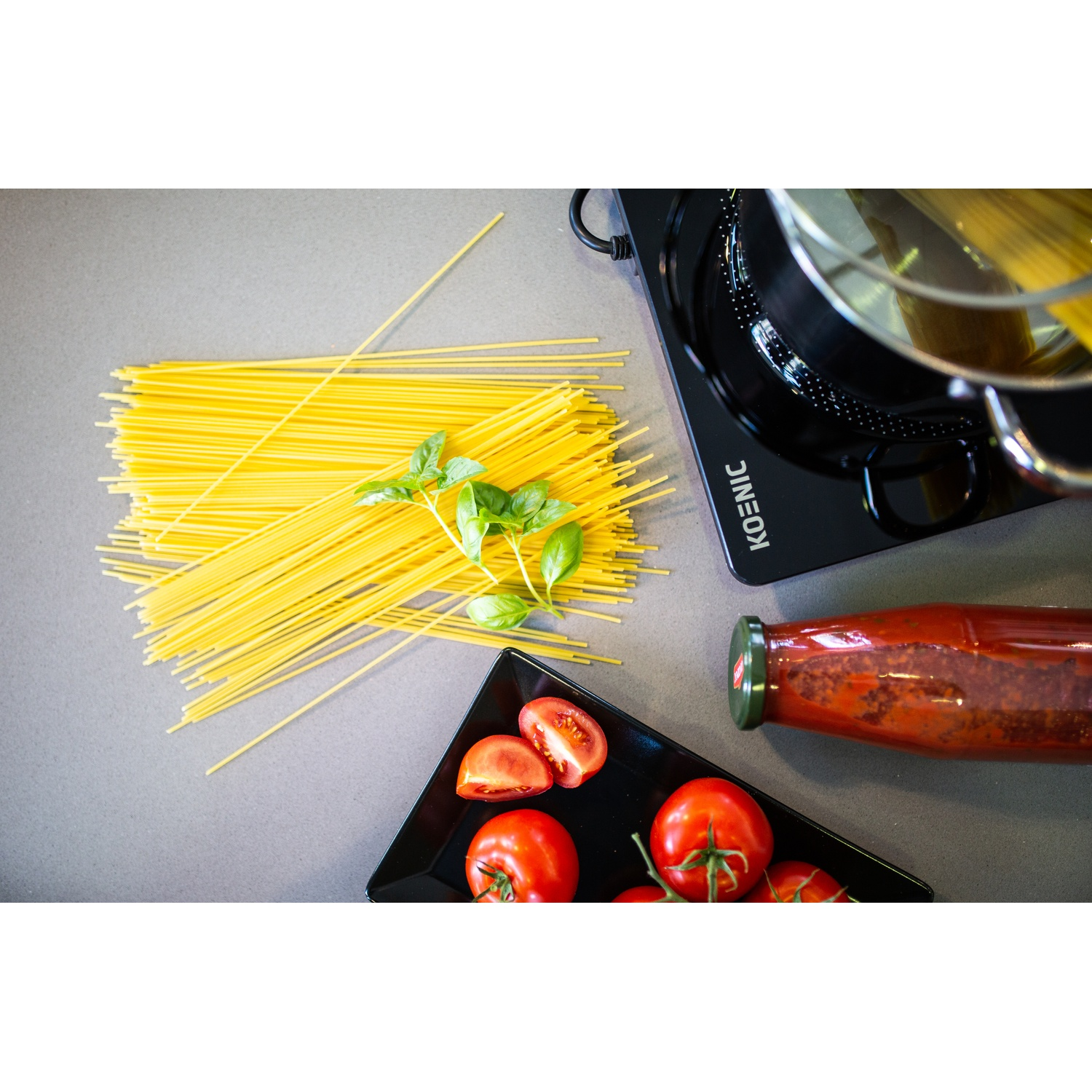 Spaghetti, tomatoes, basil, a bottle of sauce, and a pot on a hot plate.
