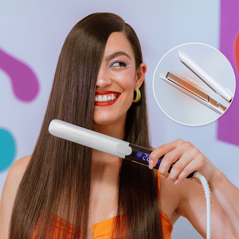 Una mujer sonriente alisa su cabello castaño largo con una plancha blanca.
