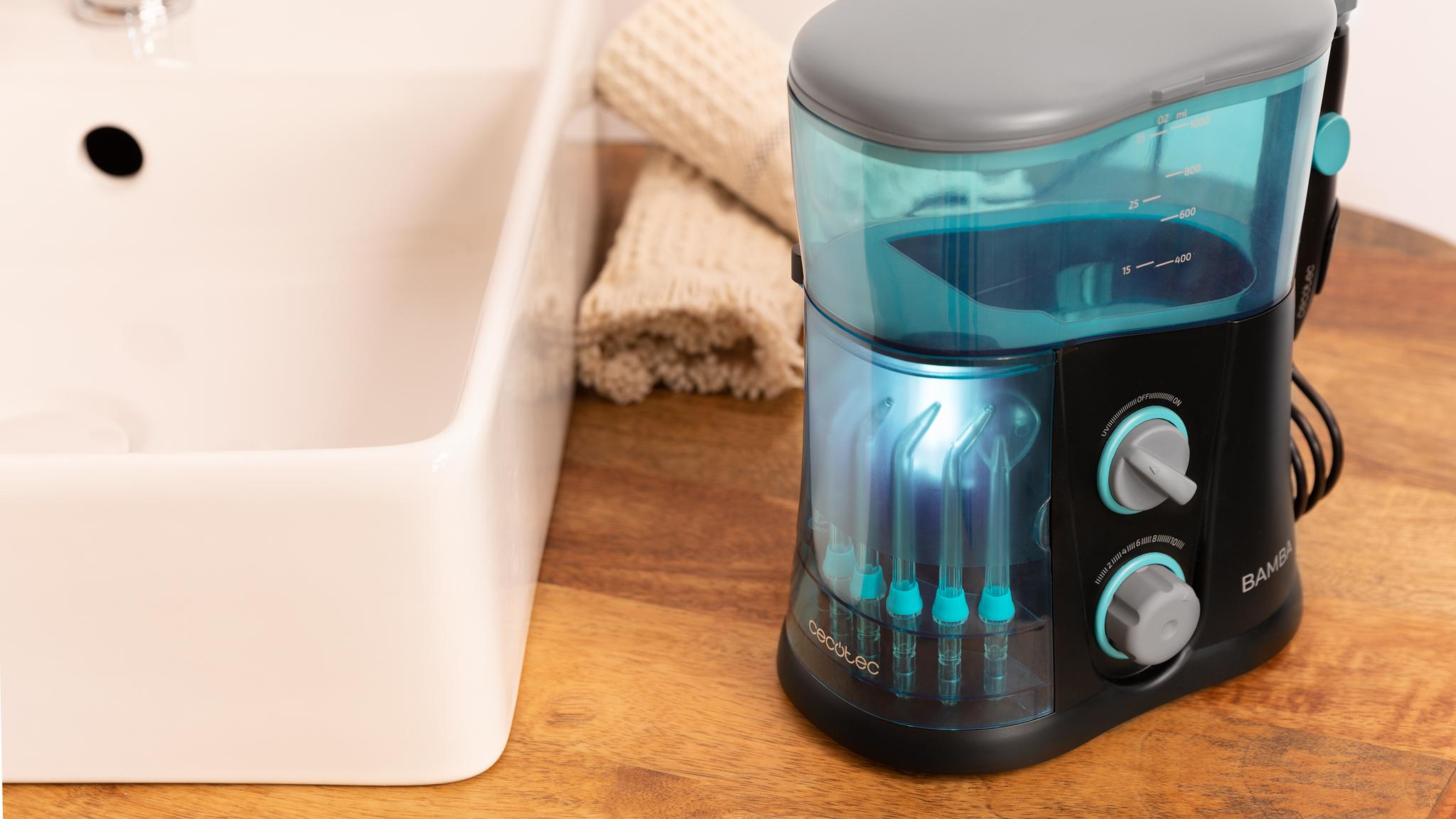 Irrigador bucal azul en mesa de madera junto a lavabo y toallas.