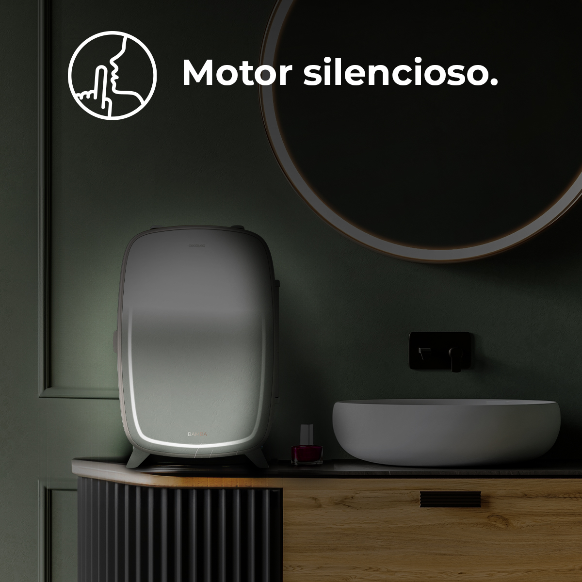 Un caliatoallas gris se encuentra en un tocador oscuro al lado de un lavabo blanco y un espejo redondo.