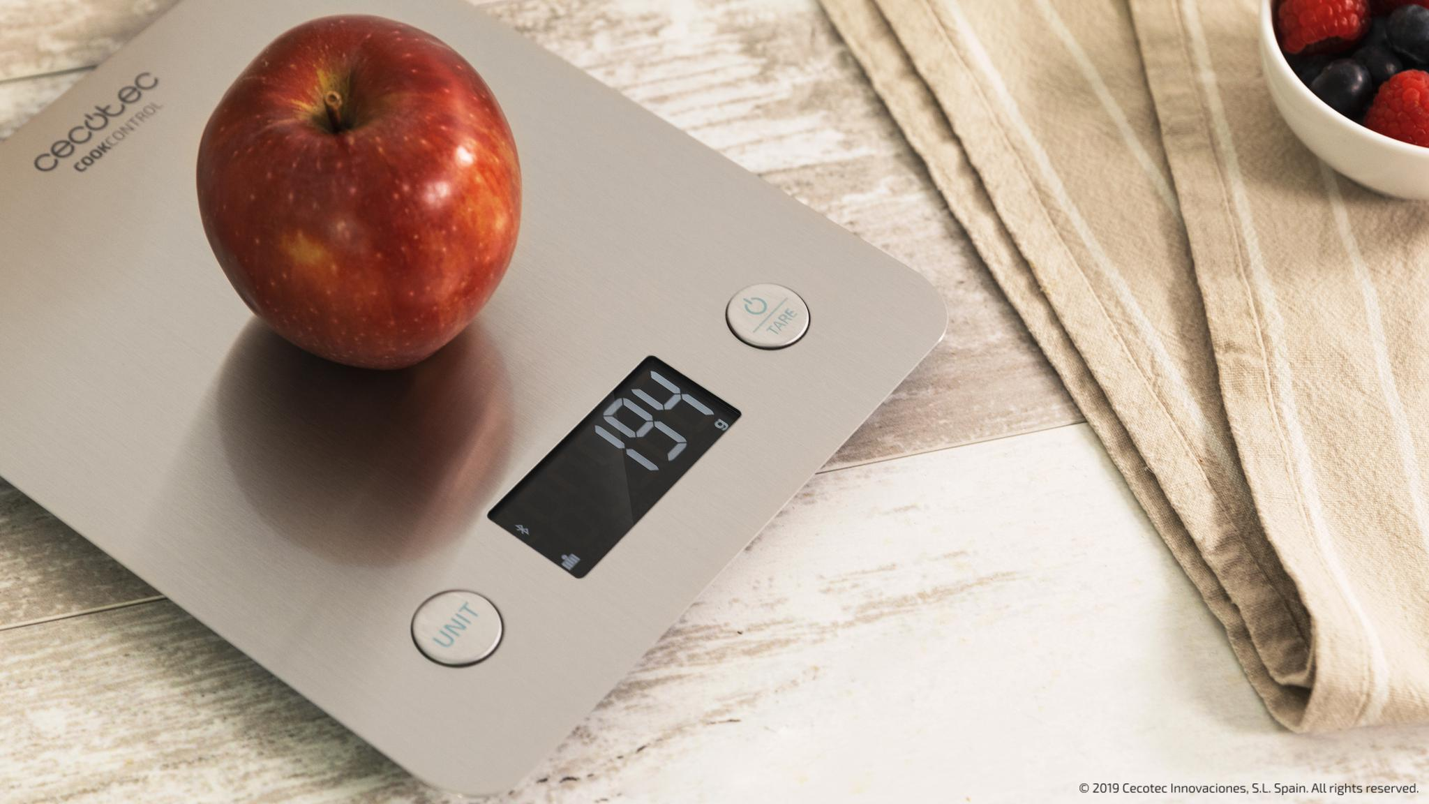 Una manzana roja en una báscula de cocina digital que muestra 194g sobre una mesa de madera.