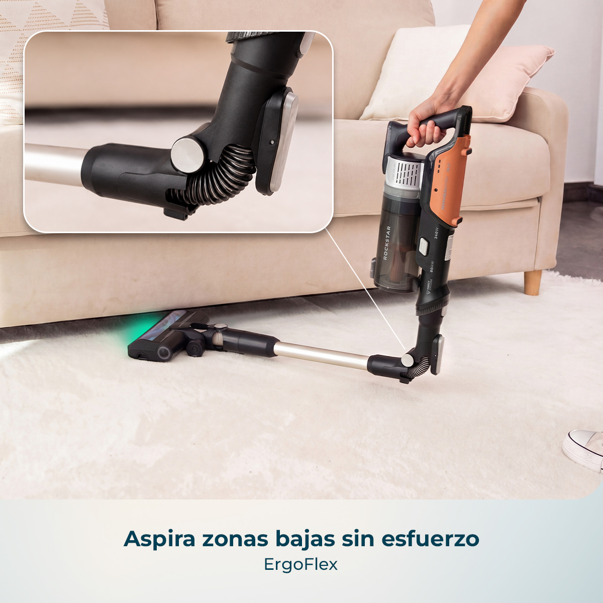 Una aspiradora sin cable con junta flexible limpia debajo de un sofá, con detalle del pliegue en un recuadro.