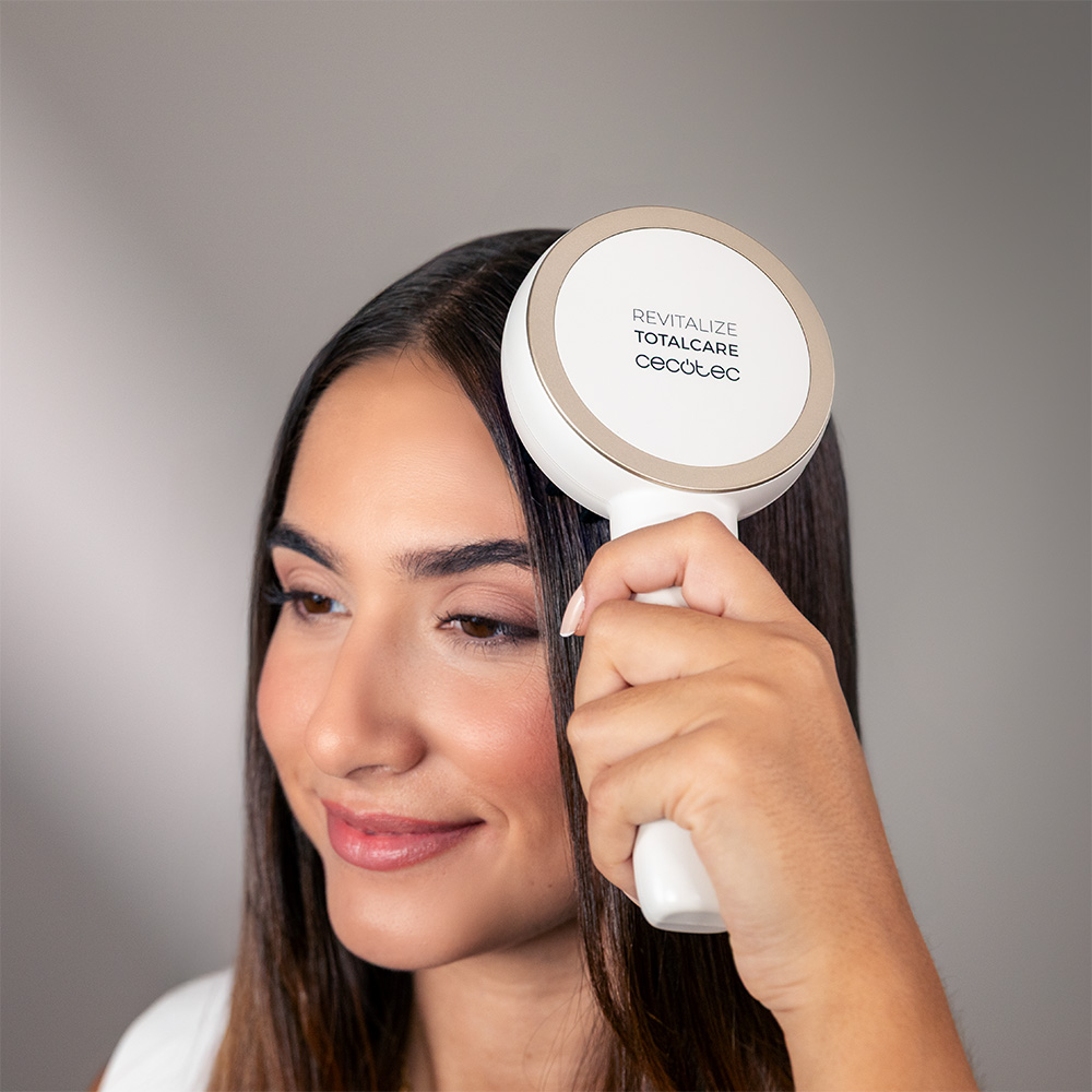 Una mujer sostiene un dispositivo para el cabello Cecotec Revitalize Totalcare blanco y dorado.
