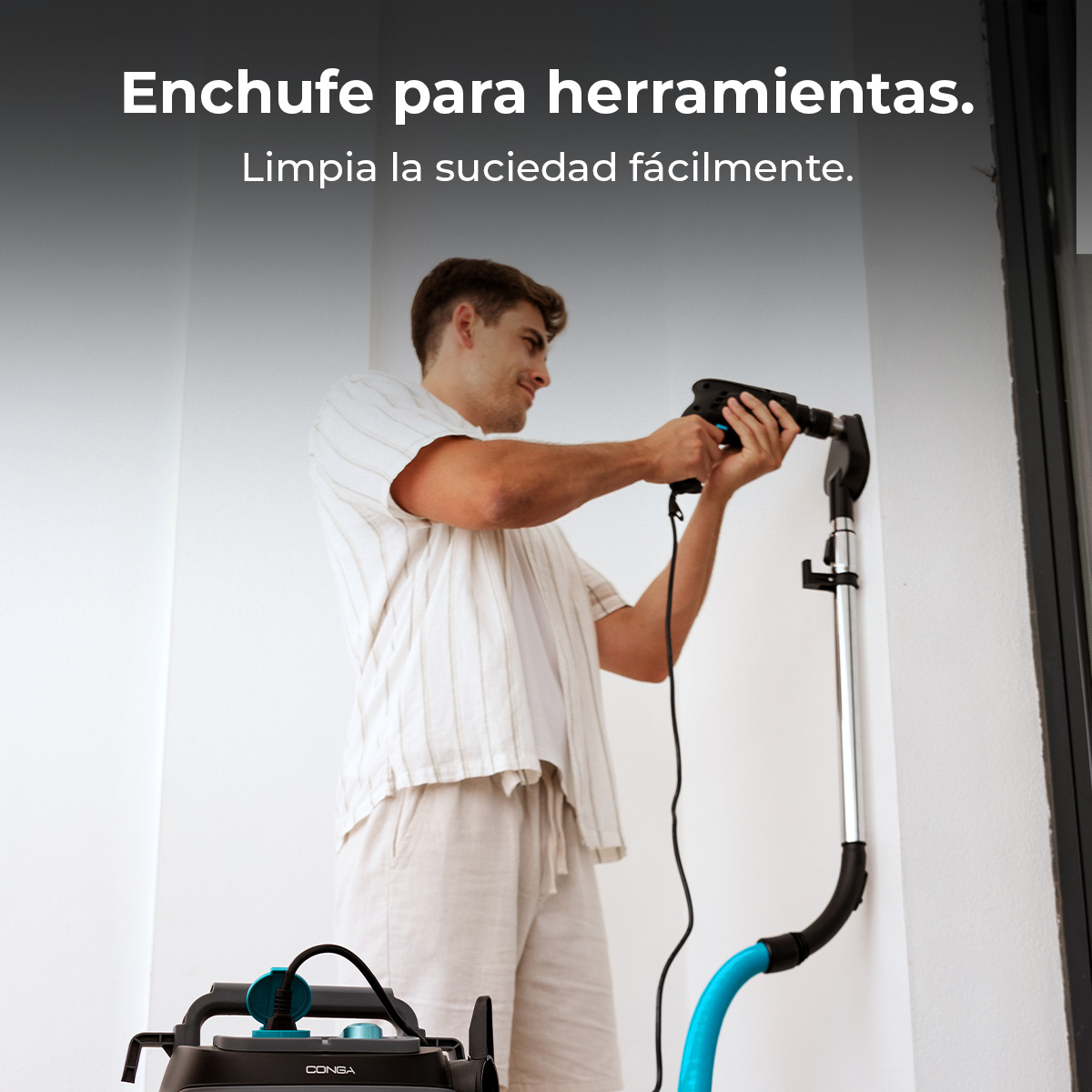 Un hombre taladra una pared sosteniendo un accesorio de aspiradora para recoger el polvo.