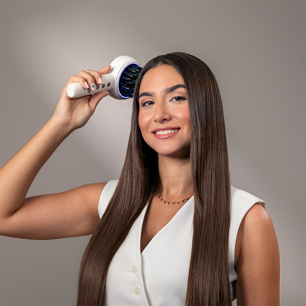 Una mujer sonriente con largo cabello castaño sostiene un cepillo blanco en su cabeza.