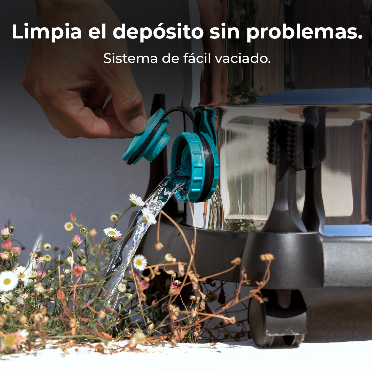 Mano abre la válvula de drenaje azul de un depósito metálico, agua fluye hacia pequeñas flores blancas y rosas.