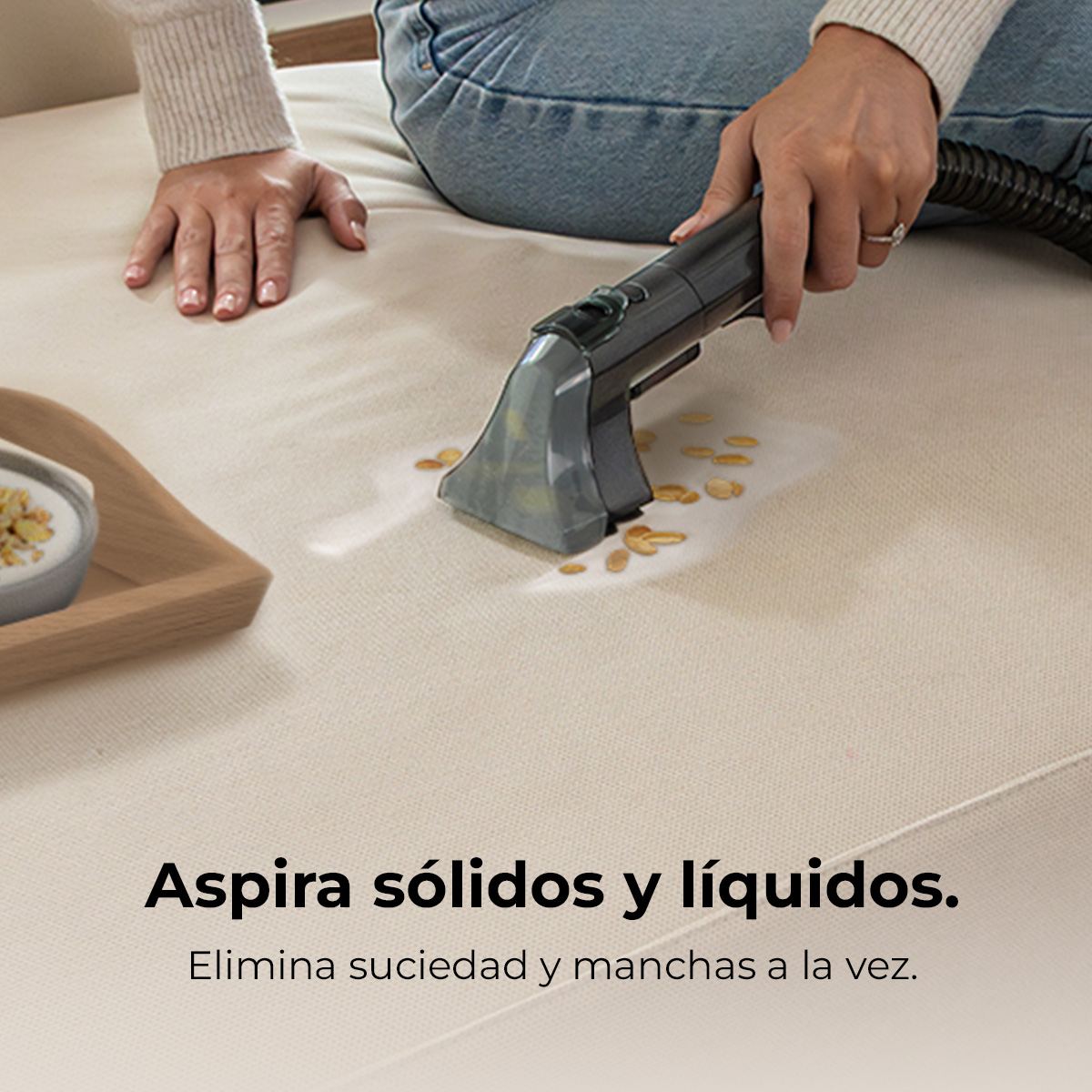 Persona aspira suciedad líquida y restos de comida de un sofá claro.