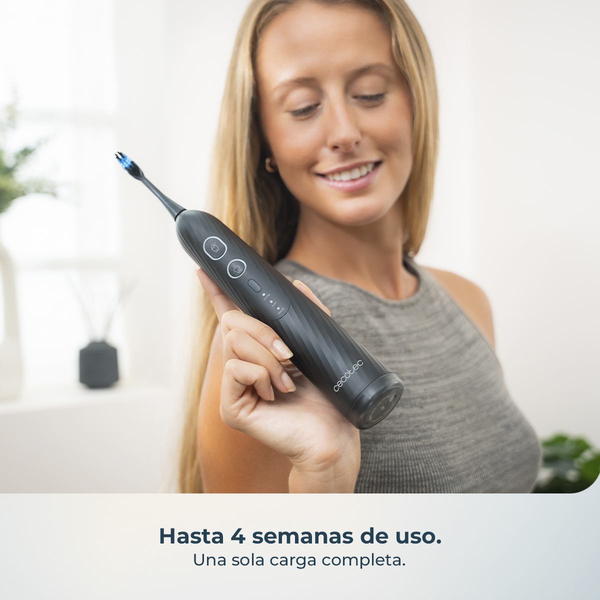 Una mujer rubia sonriente sostiene un cepillo de dientes eléctrico negro.