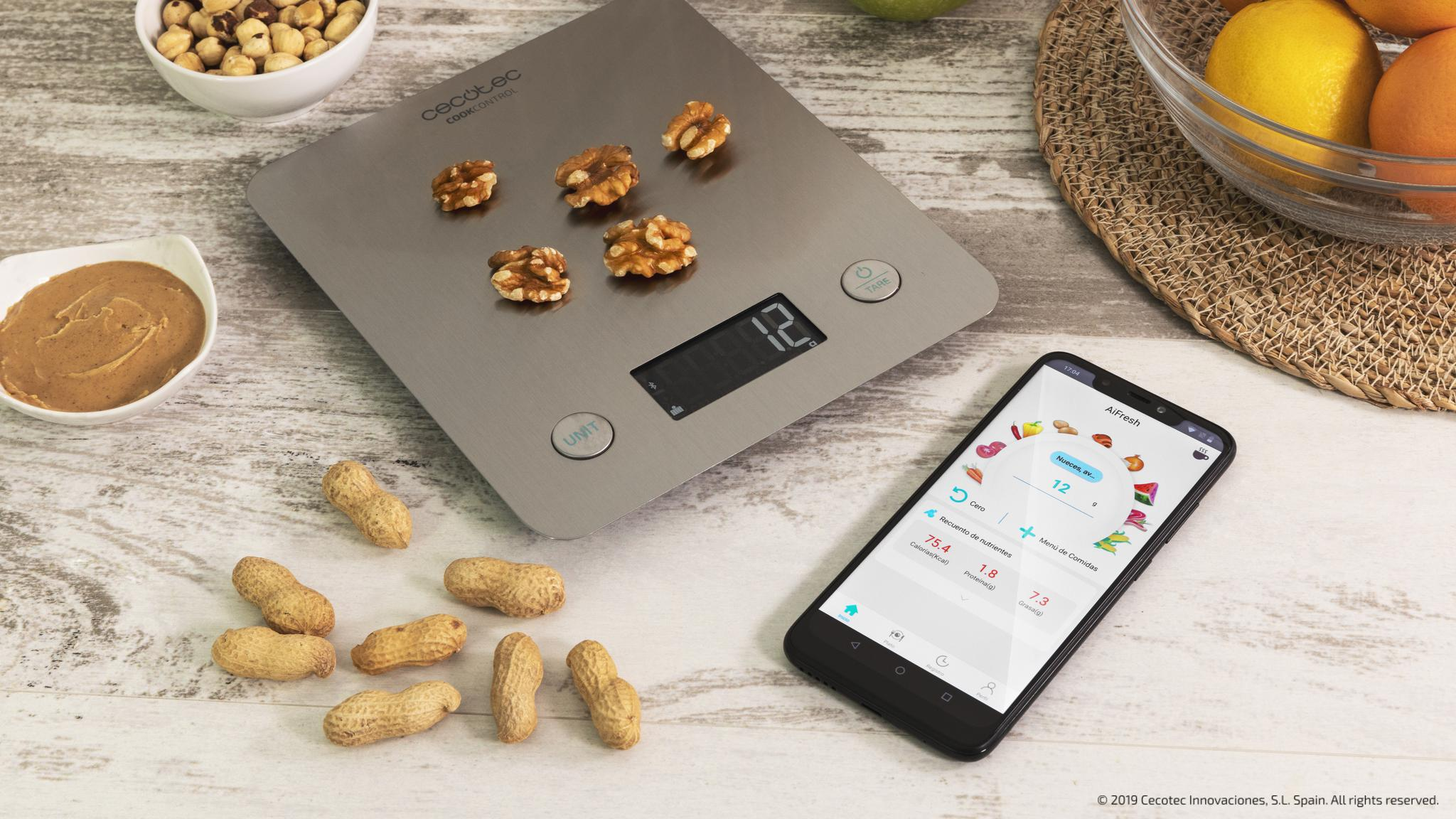 Una balanza de cocina digital con nueces, un smartphone con una aplicación, cacahuetes y un bol en la mesa.