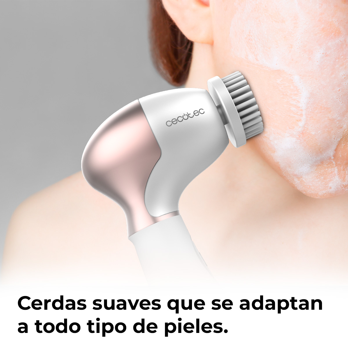 Un cepillo limpiador facial blanco y oro rosa limpia suavemente una mejilla con jabón.
