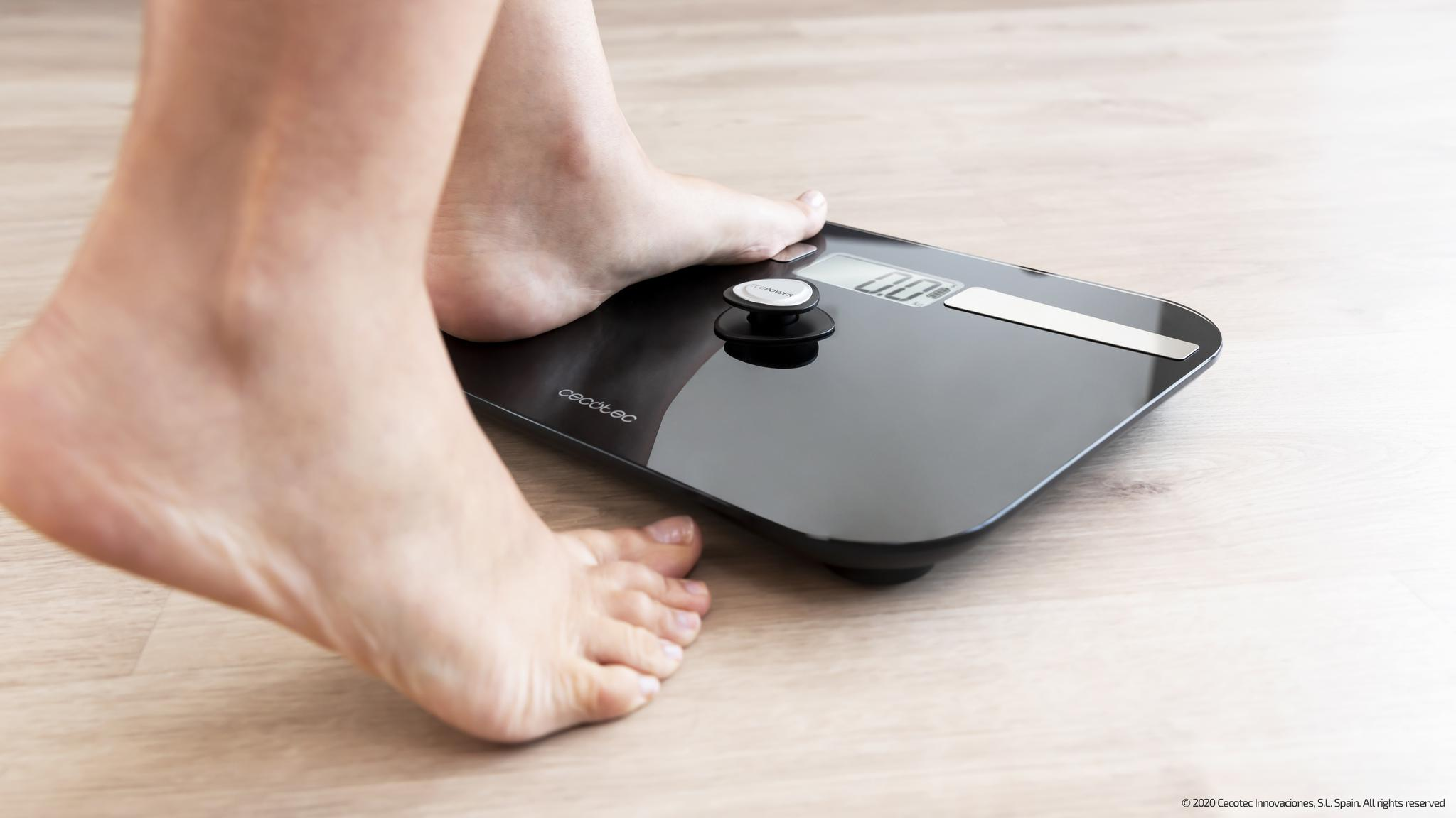 Pies descalzos sobre una báscula digital negra en suelo de madera.