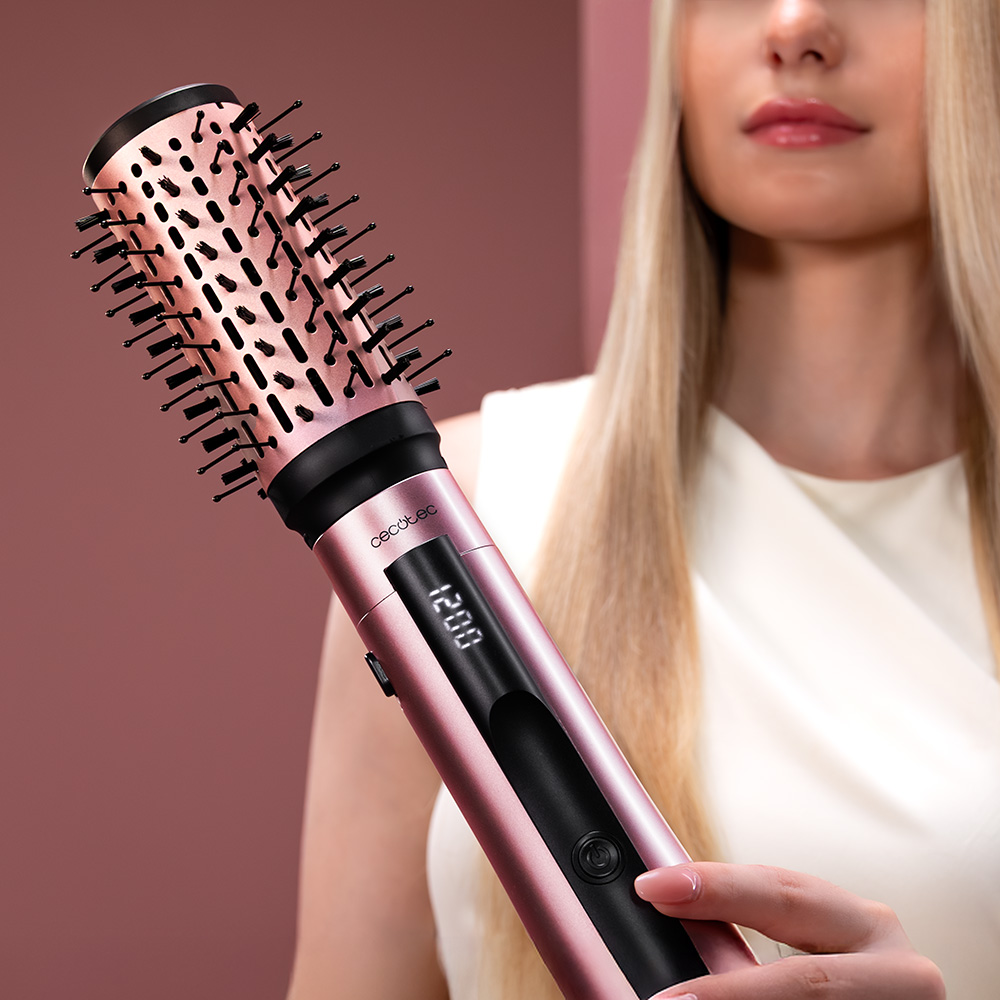 Una mujer rubia sostiene un cepillo de aire caliente rosa con pantalla digital.