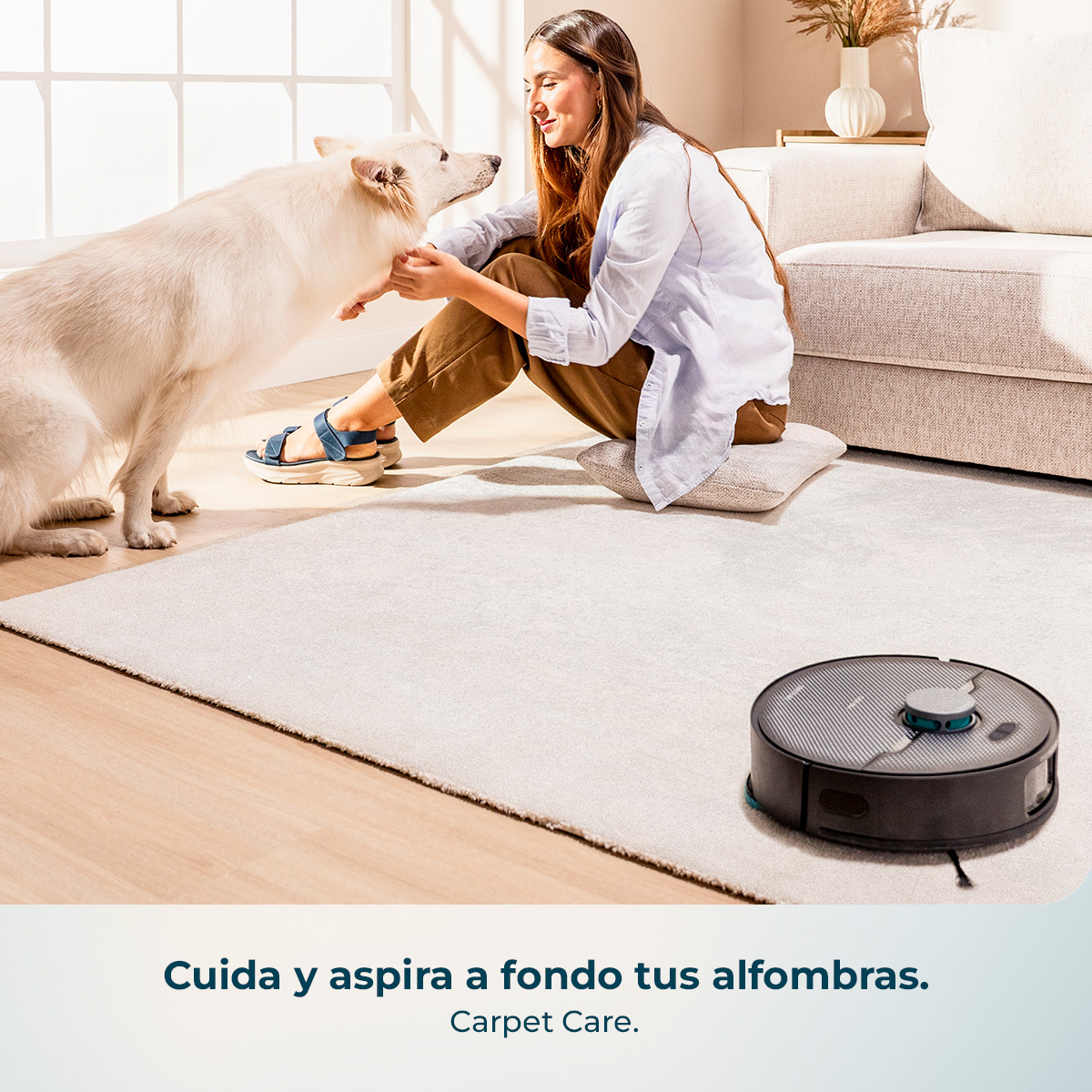 Una mujer sentada en una alfombra acaricia a un perro blanco, mientras un robot aspirador está cerca.