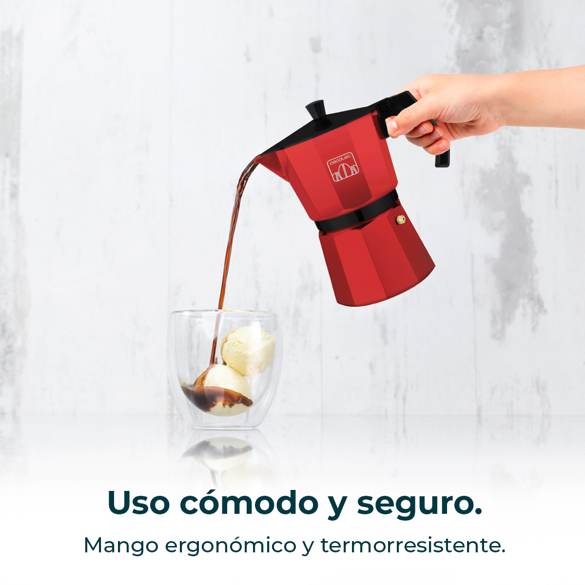 Una mano vierte café de una cafetera italiana roja en un vaso con bolas de helado sobre fondo claro.