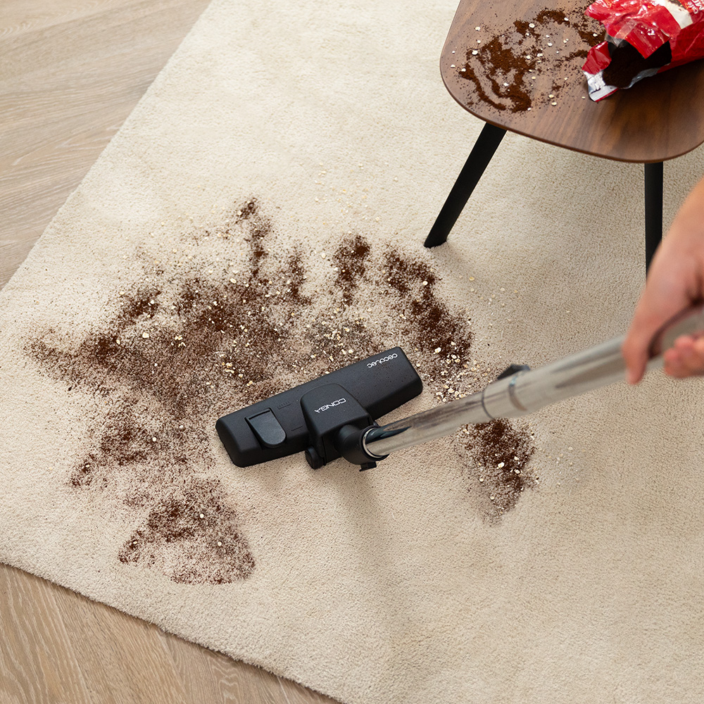 Una aspiradora limpia posos de café y avena de una alfombra beige.