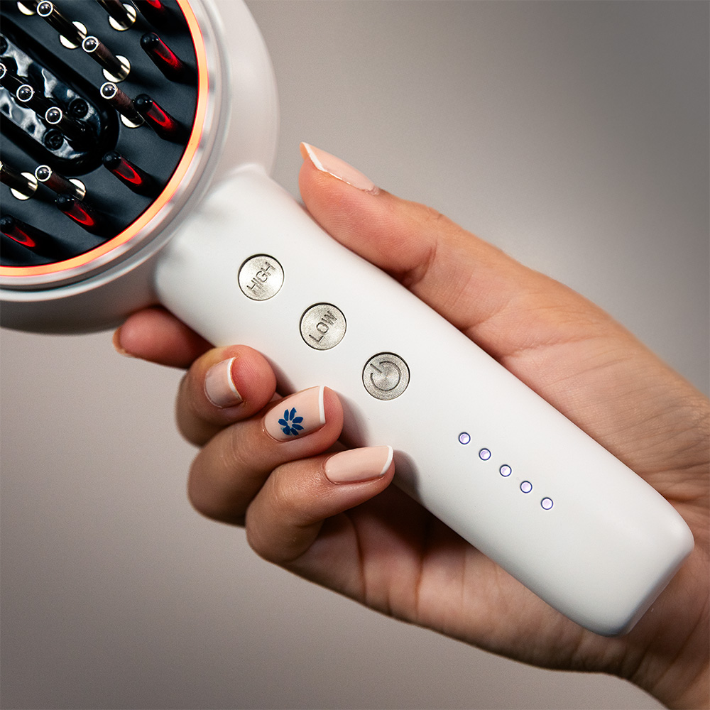 Una mano sostiene un cepillo de pelo blanco con botones y luces indicadoras.
