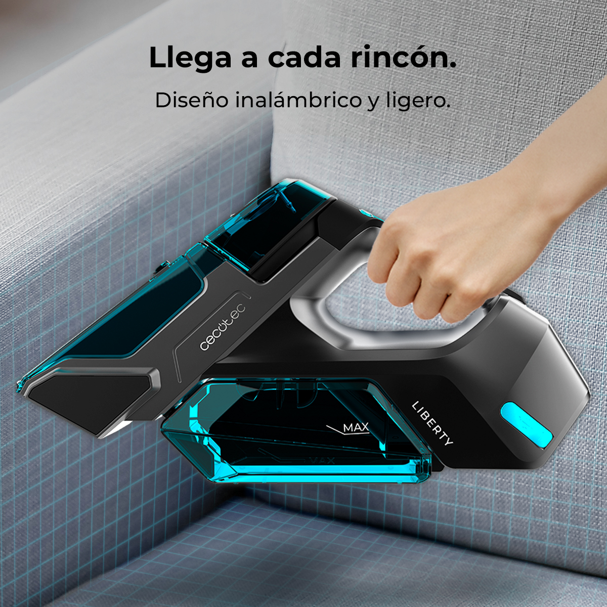 Una mano sostiene un aspirador de mano Cecotec Liberty negro y azul sobre un sofá gris.