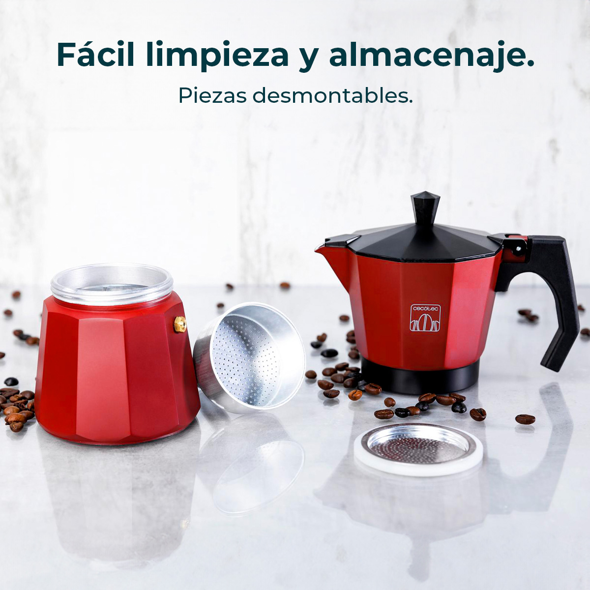Cafetera moka roja desmontada con granos de café esparcidos sobre una superficie gris.